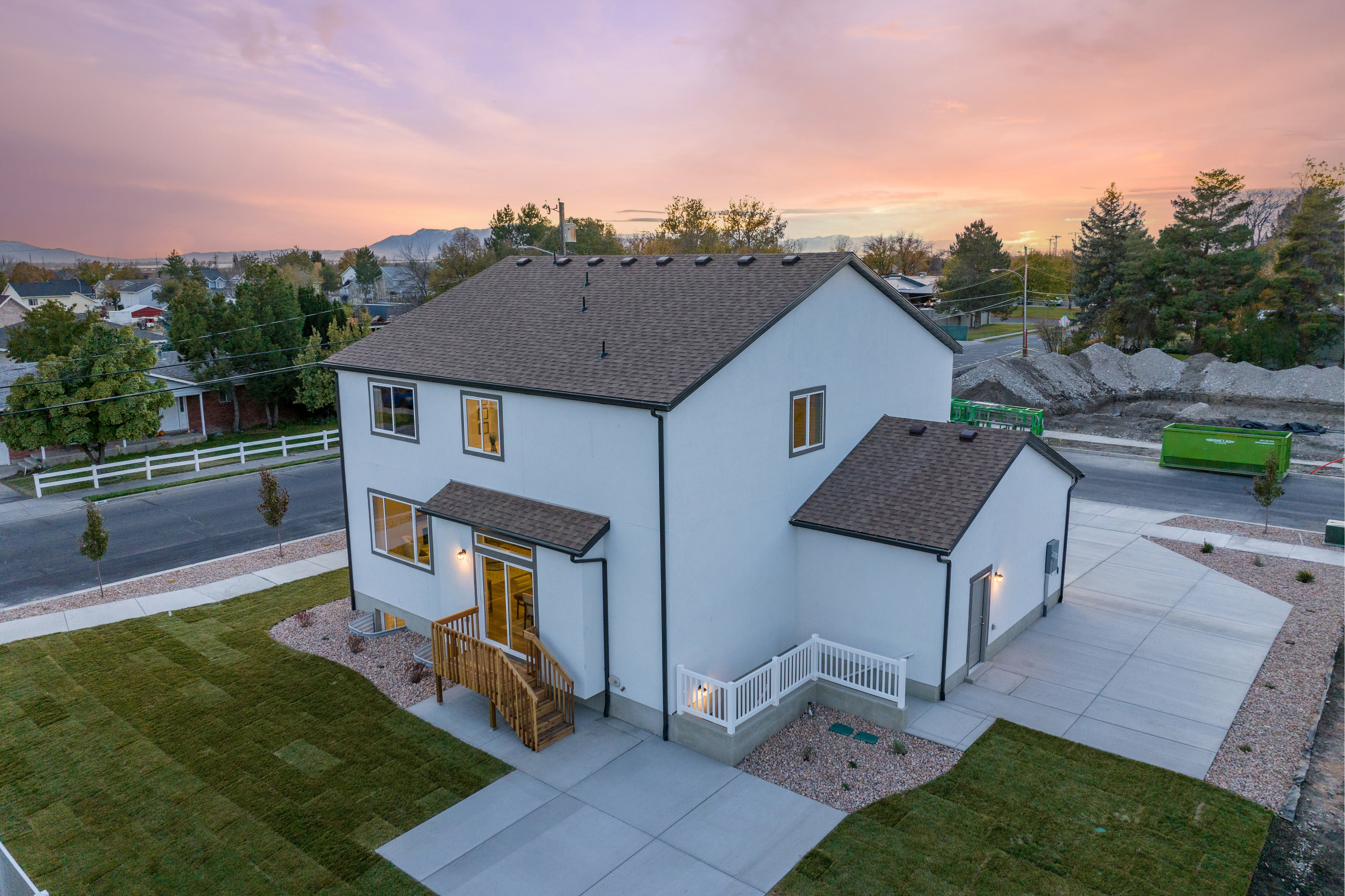 Contemporary two-story residence featuring a white stucco exterior with black trim, a dark shingle roof, and multiple large windows