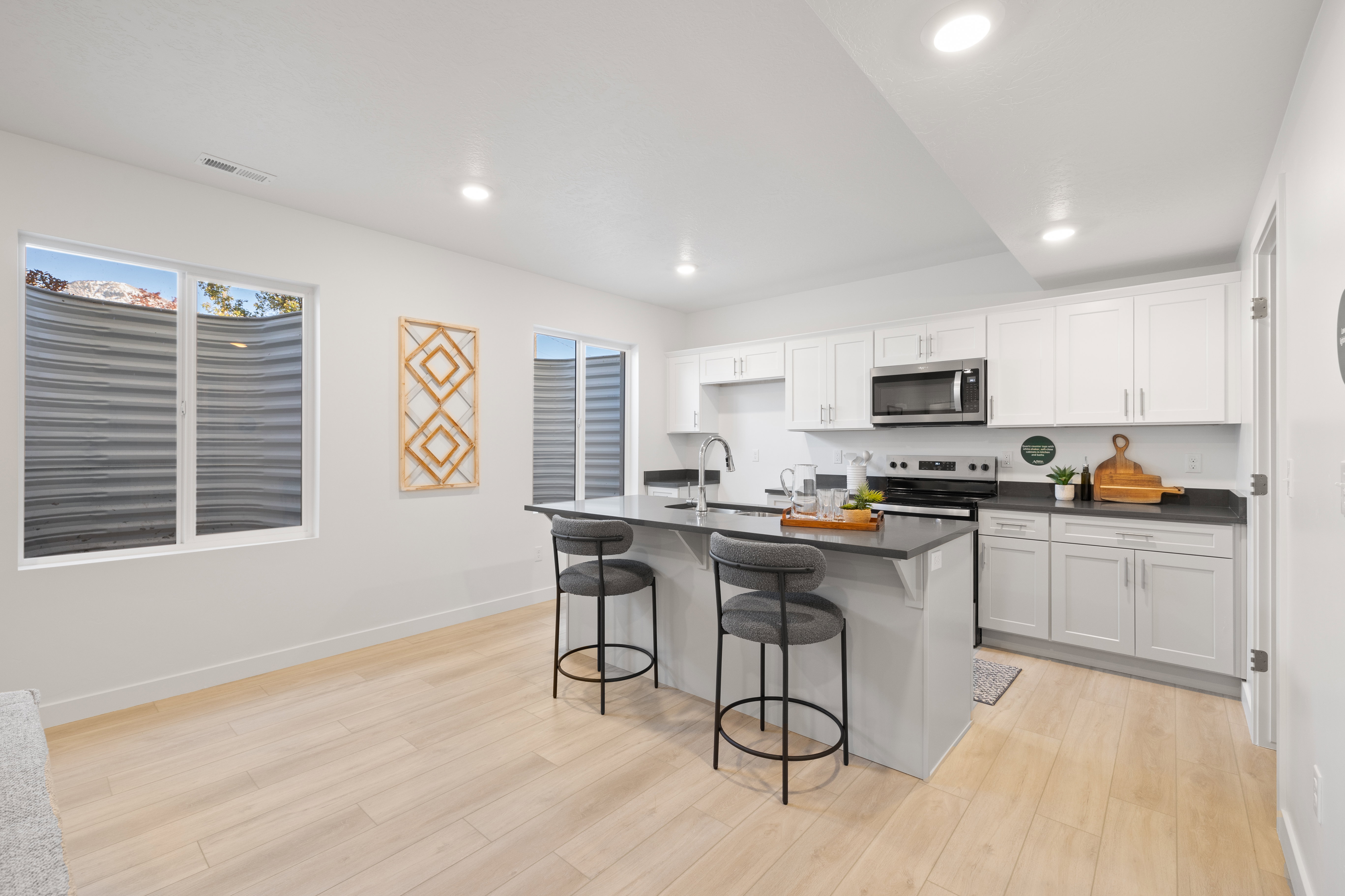 Modern kitchen featuring light wood-finish flooring, white cabinetry with brushed nickel hardware, and dark countertops