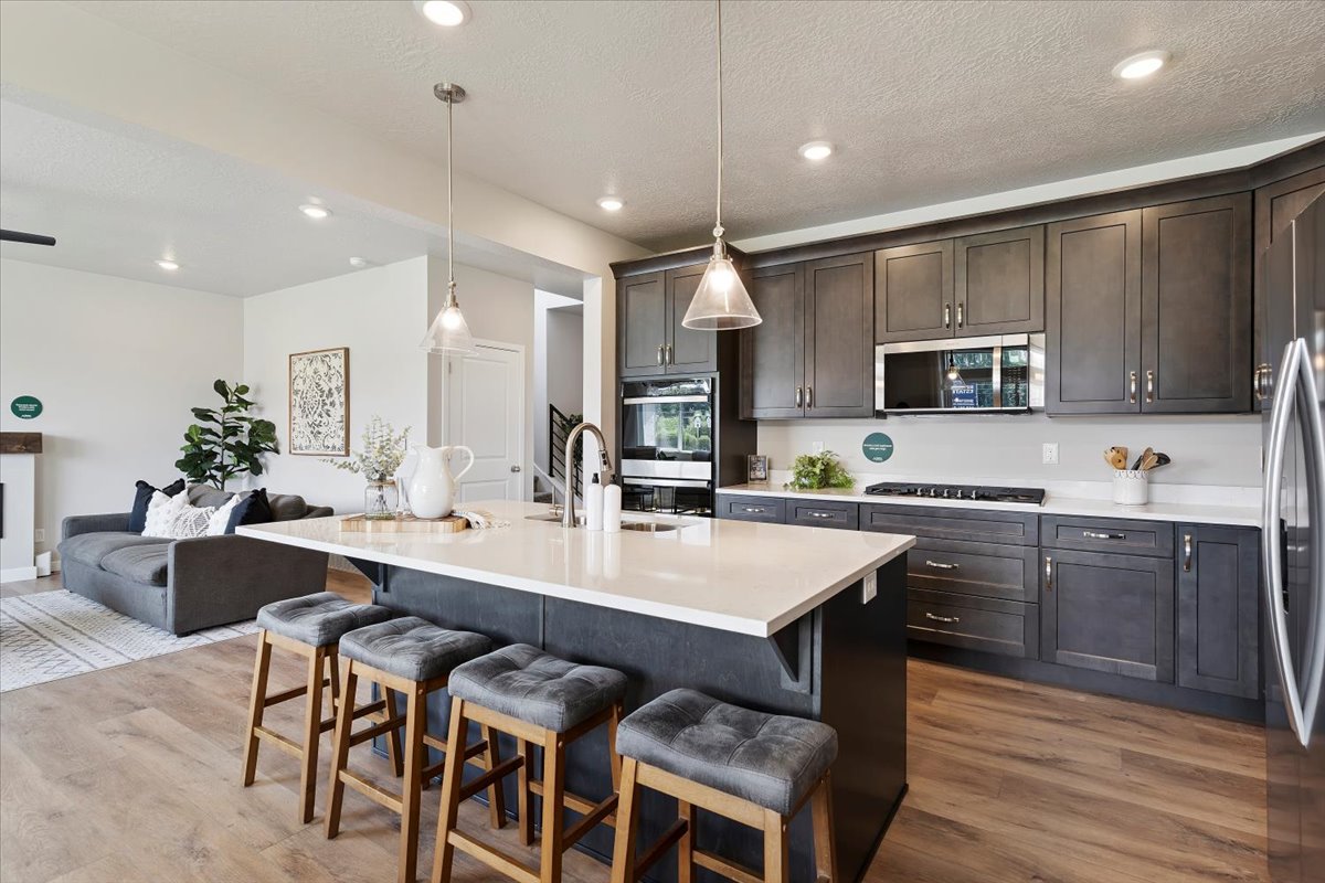 Open-concept kitchen featuring an island with integrated sink, stainless steel appliances, dark wood-finish cabinetry, and light countertops