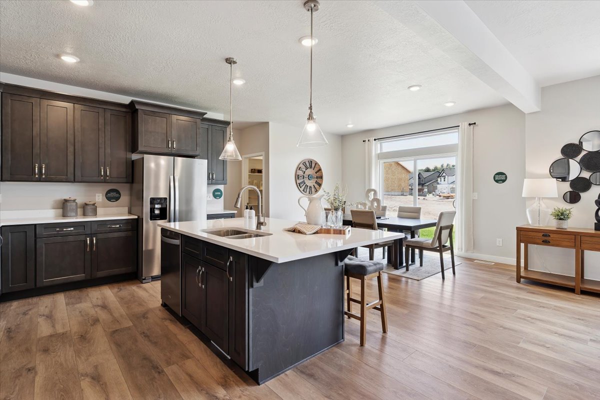 Open-concept kitchen featuring an oversized island with seating, stainless steel appliances, dark wood cabinetry, white countertops, and wood-finish flooring