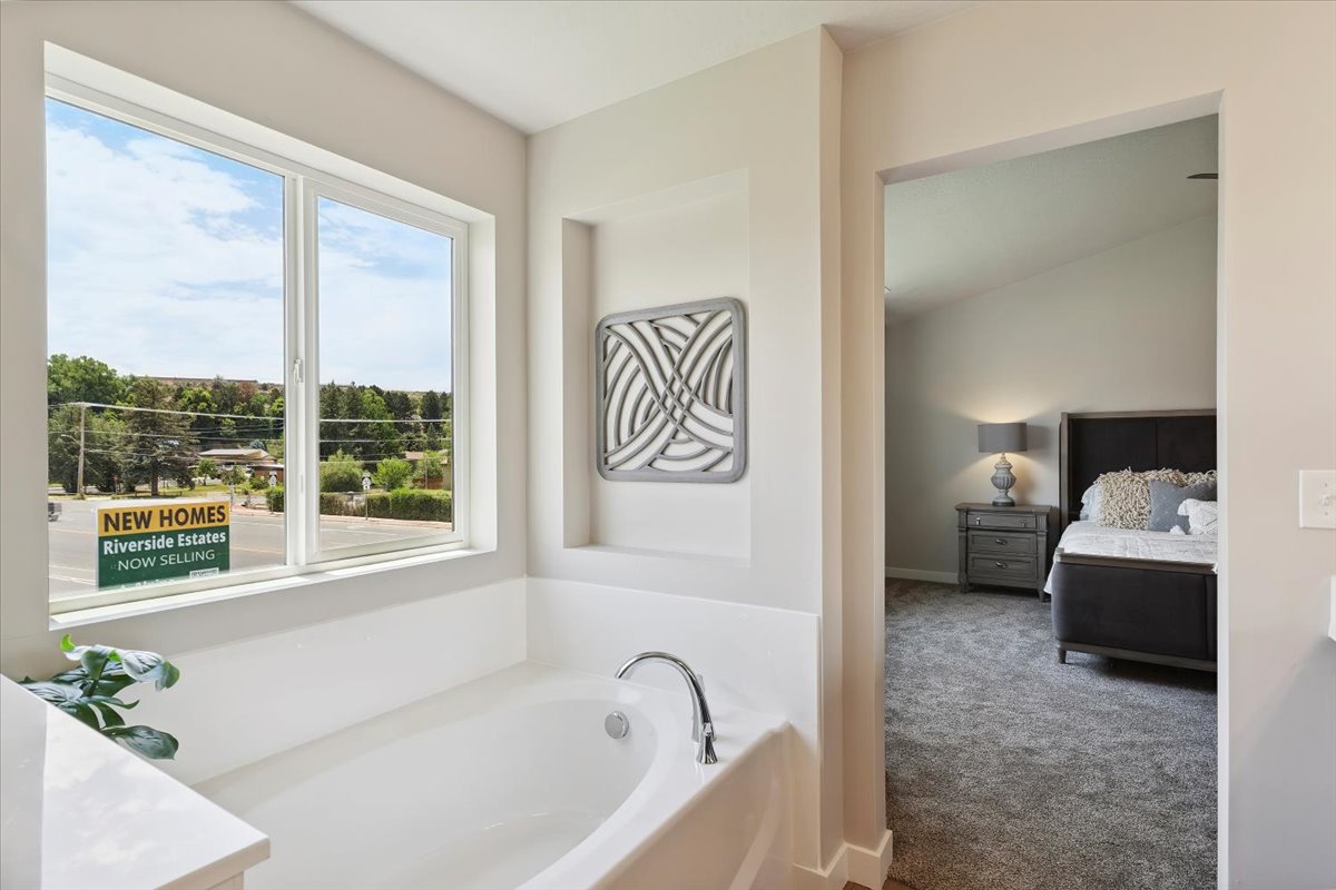 Deep soaking tub with chrome fixtures, integrated wall niche, and a large window