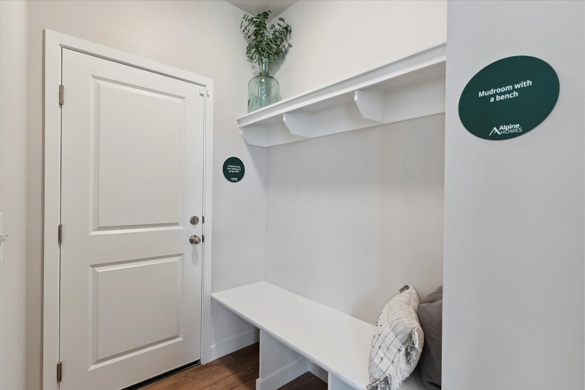 Mudroom featuring a built-in bench, upper shelf with corbel details, white paneled door with brushed nickel hardware, and wood-finish flooring