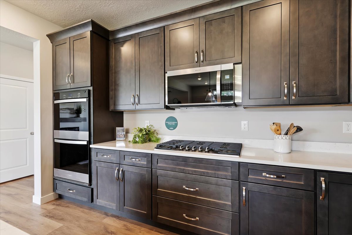 Contemporary kitchen featuring dark wood-finish cabinetry, light-toned countertops, a stainless steel microwave, and a built-in double oven