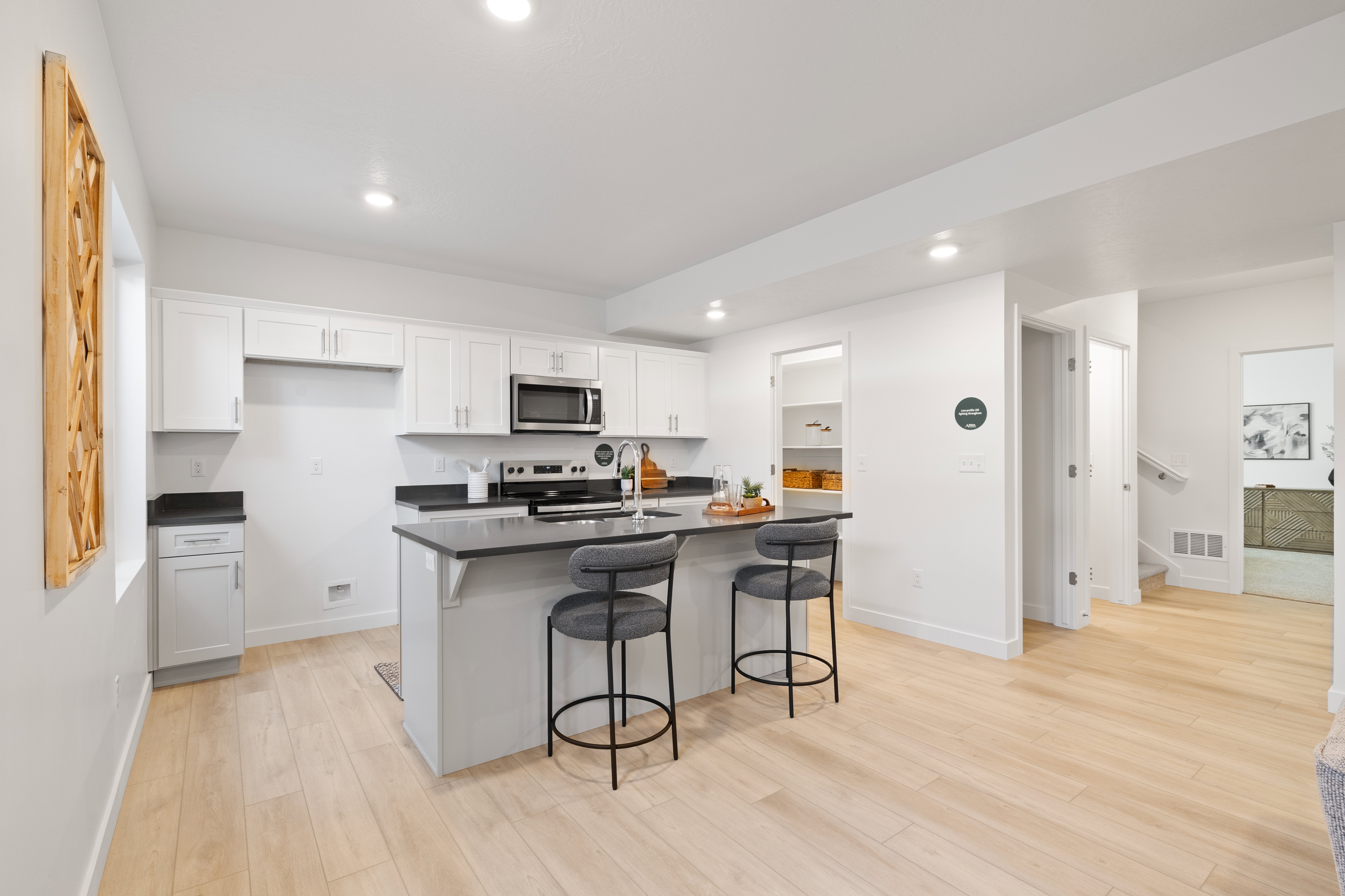 Modern kitchen featuring light wood-finish flooring, white cabinetry, dark countertops, and stainless steel appliances