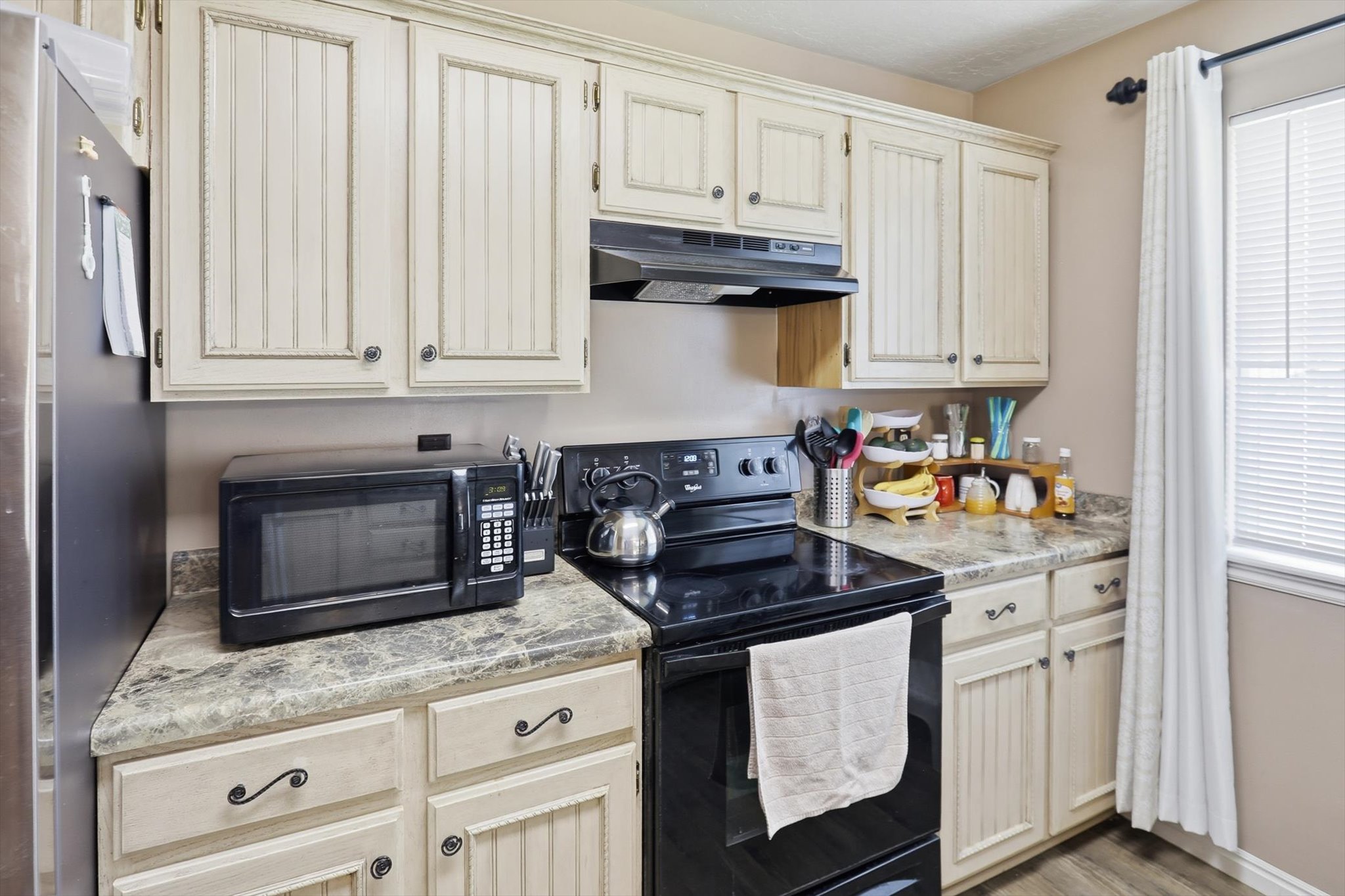 Kitchen featuring cream-colored beadboard cabinetry, dark countertops, and a black range with an overhead vent