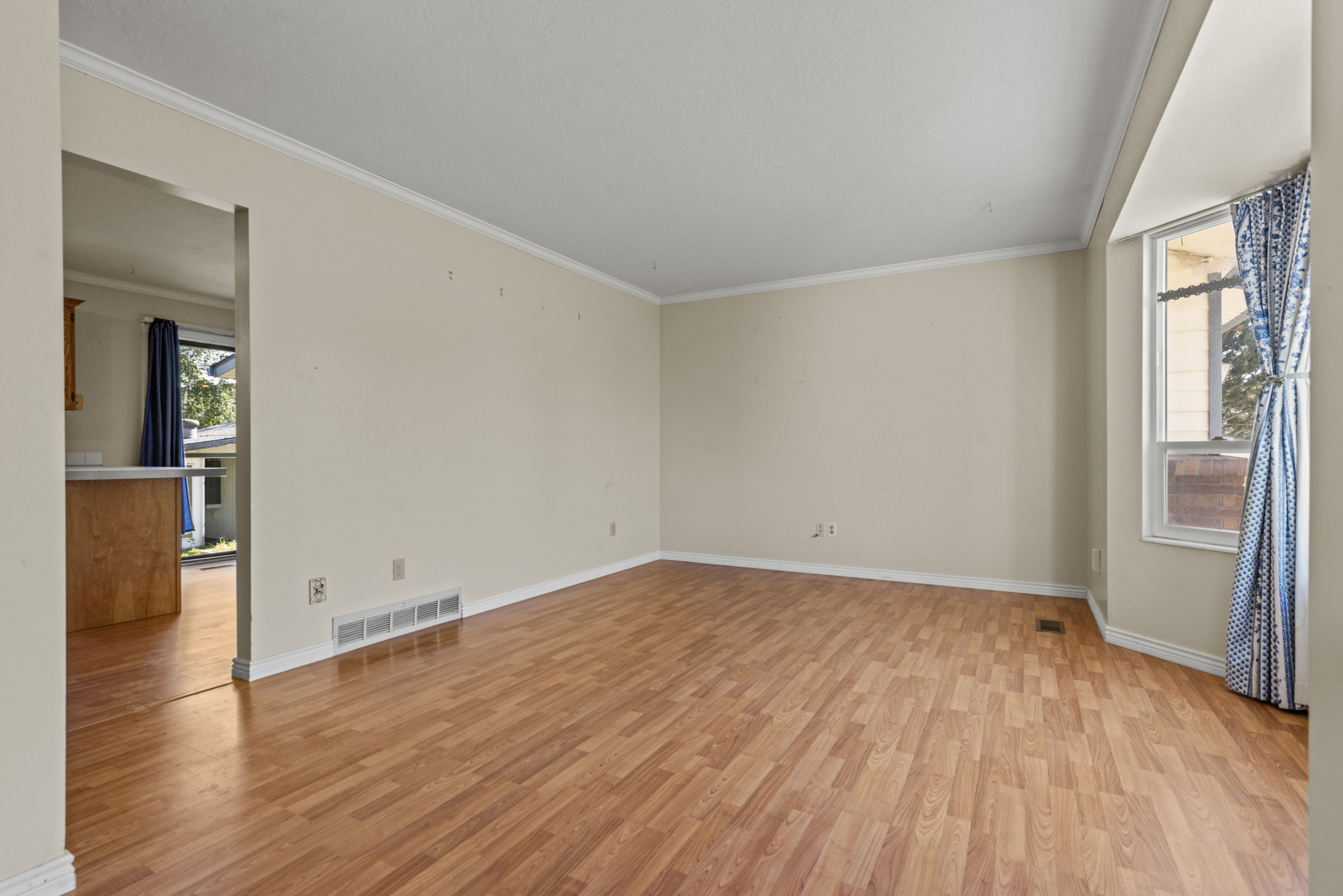 Spacious room featuring wood-finish flooring, light-toned walls, and white crown molding