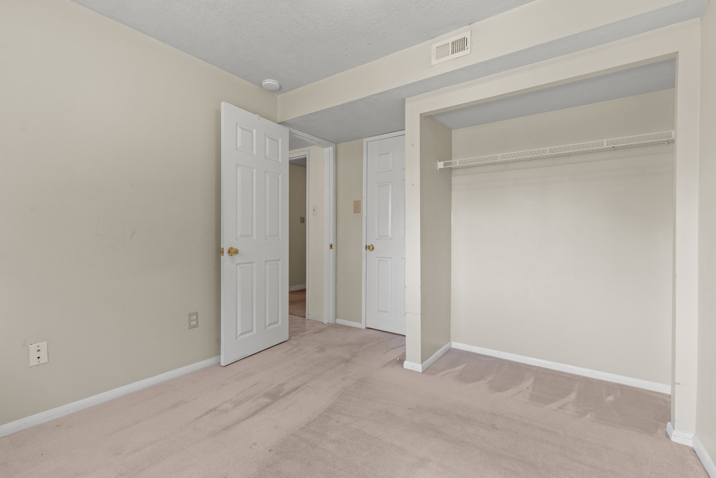 Neutral-toned room featuring wall-to-wall carpeting and an open closet space with a wire shelf and hanging rod