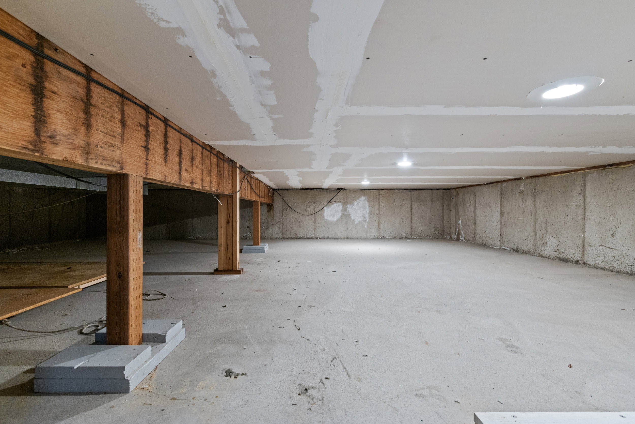 Unfinished basement featuring concrete flooring, exposed wooden support beams, and recessed lighting