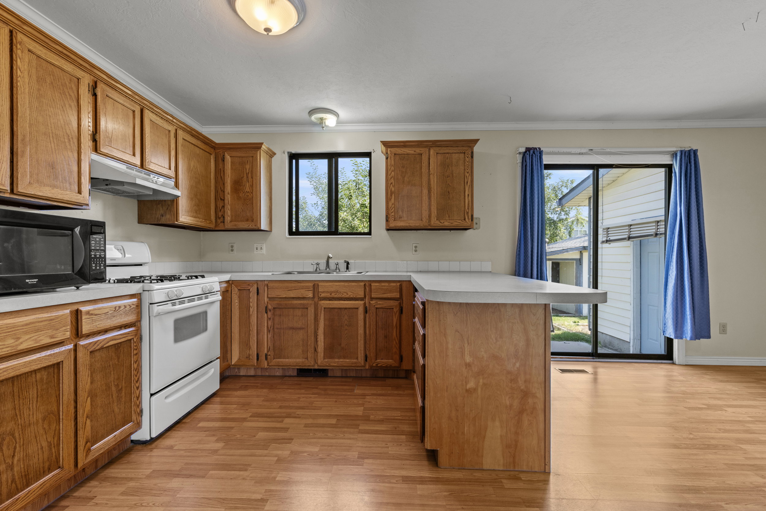 Kitchen featuring wood-finish flooring, wood cabinetry, light-toned countertops, a built-in microwave, and a gas range