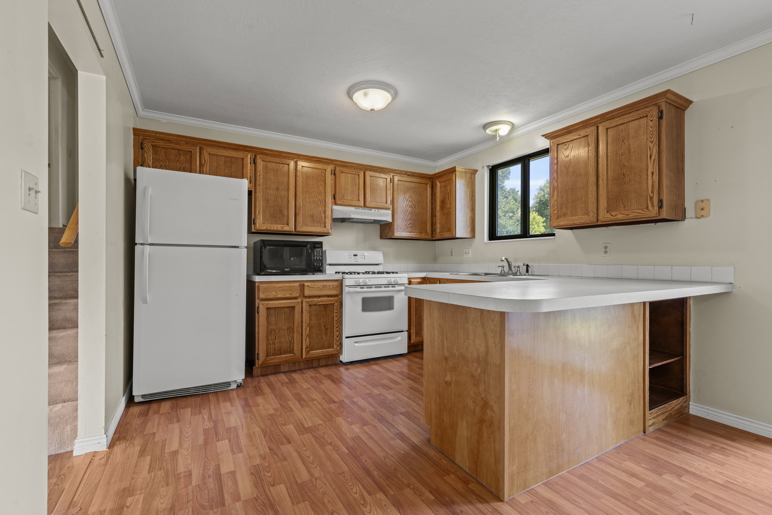 Kitchen featuring wood-finish cabinetry, white appliances, and a central island with integrated shelving