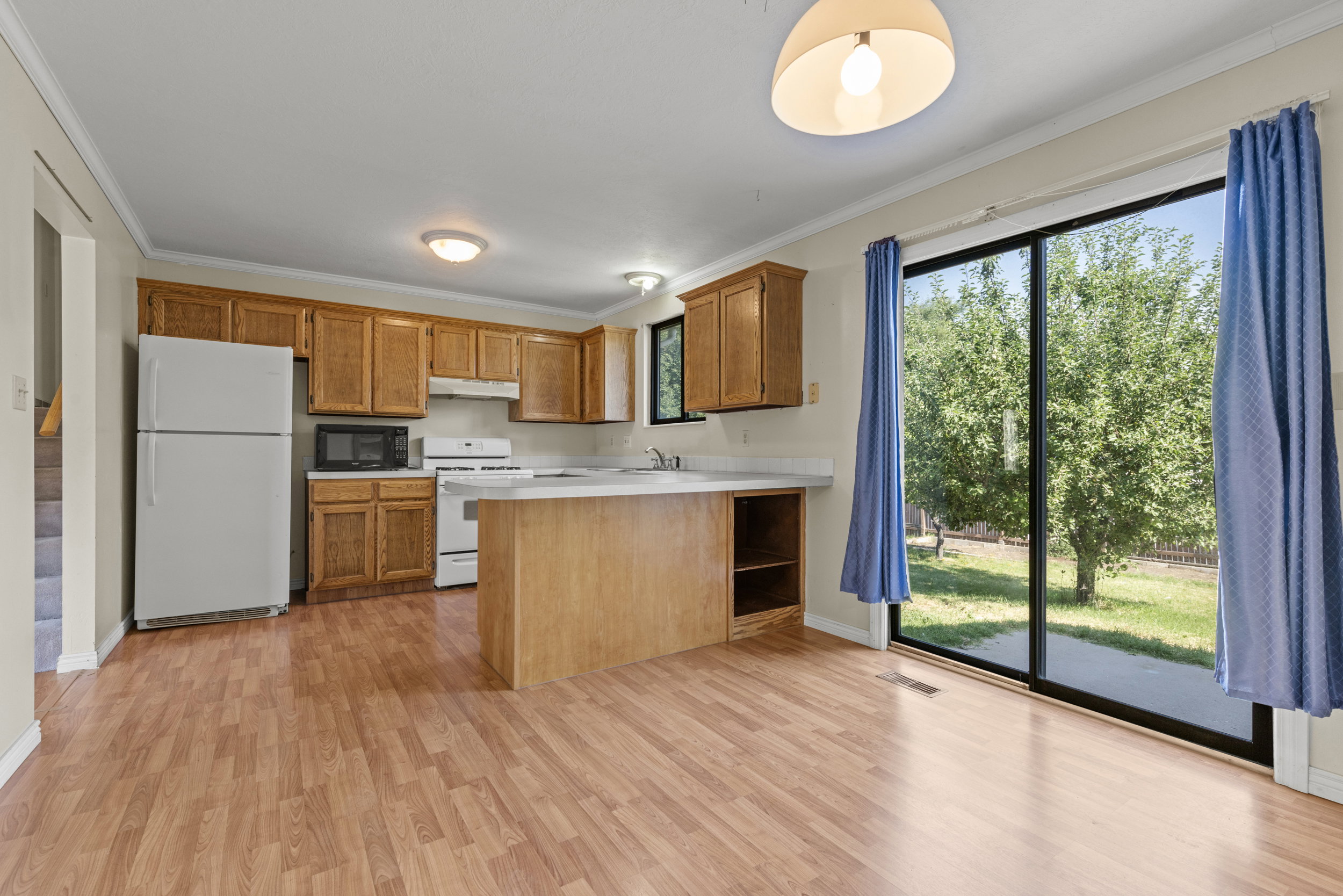 Open-concept kitchen and dining area featuring wood-finish flooring, wood cabinetry, white appliances, and a peninsula countertop