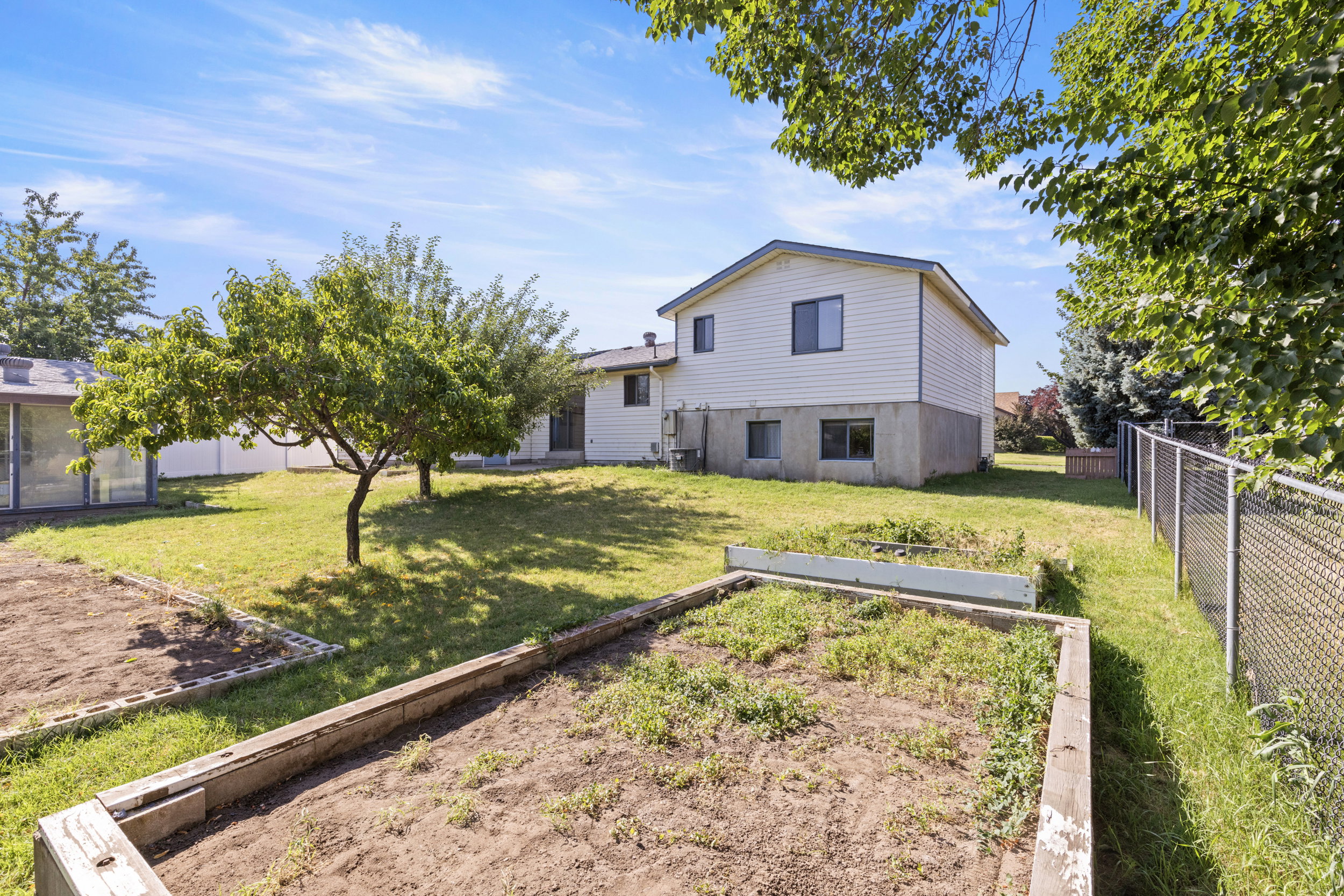 Expansive backyard featuring a chain-link fence, mature trees, and raised garden beds