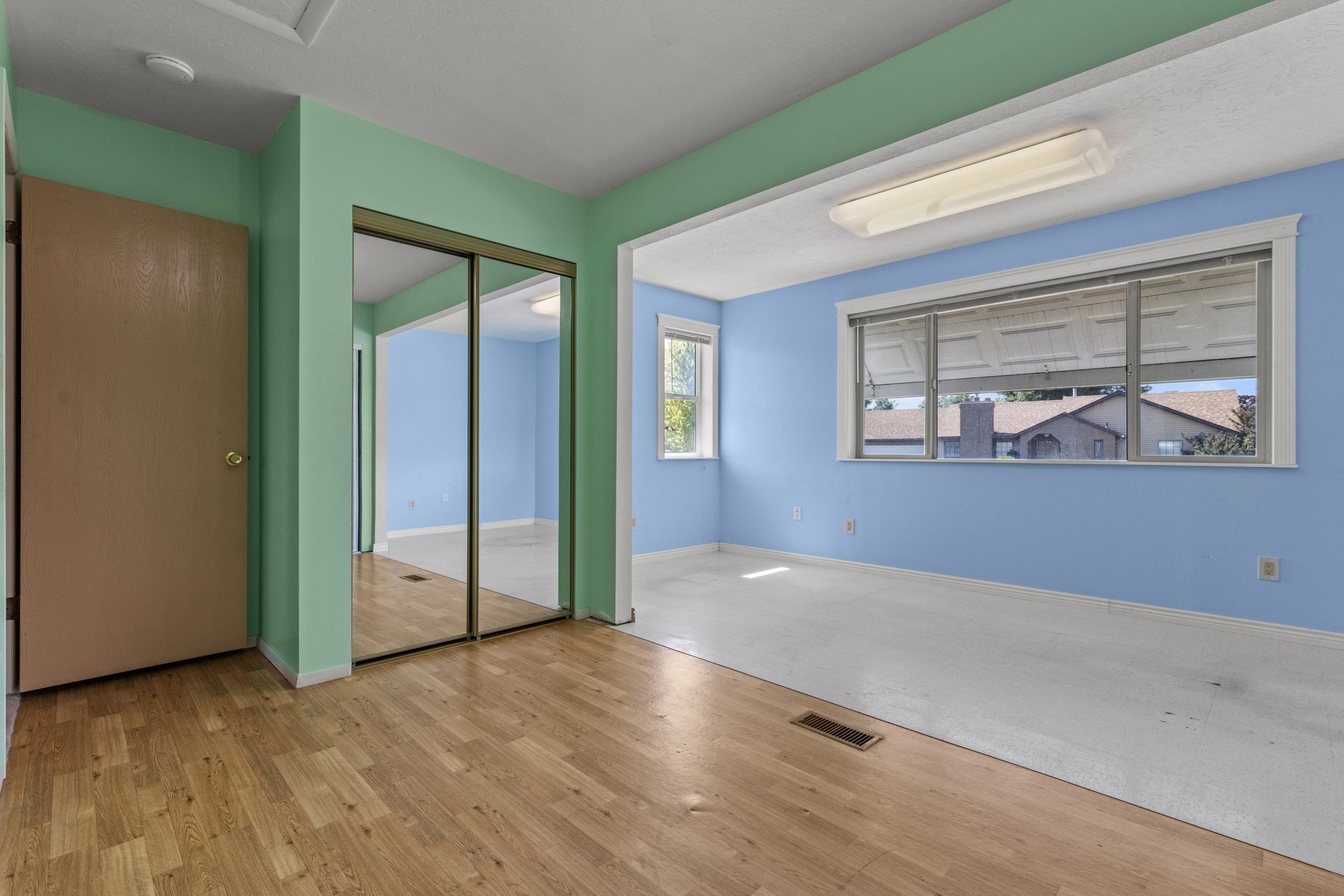 Spacious room featuring wood-finish flooring, a mirrored closet, and an expansive window