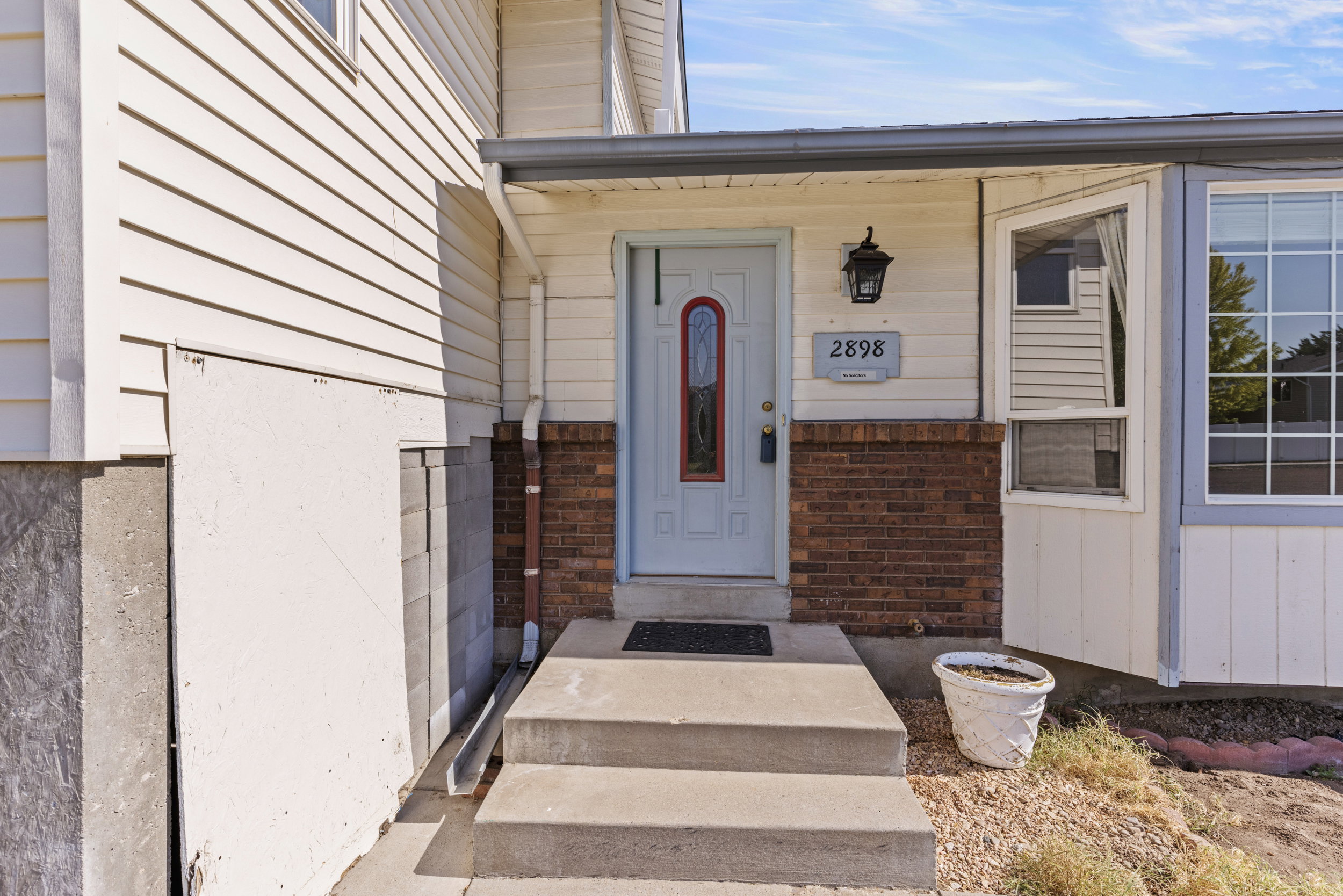 Front entry featuring a light-colored door with decorative glass, brick wainscoting, and an exterior light fixture