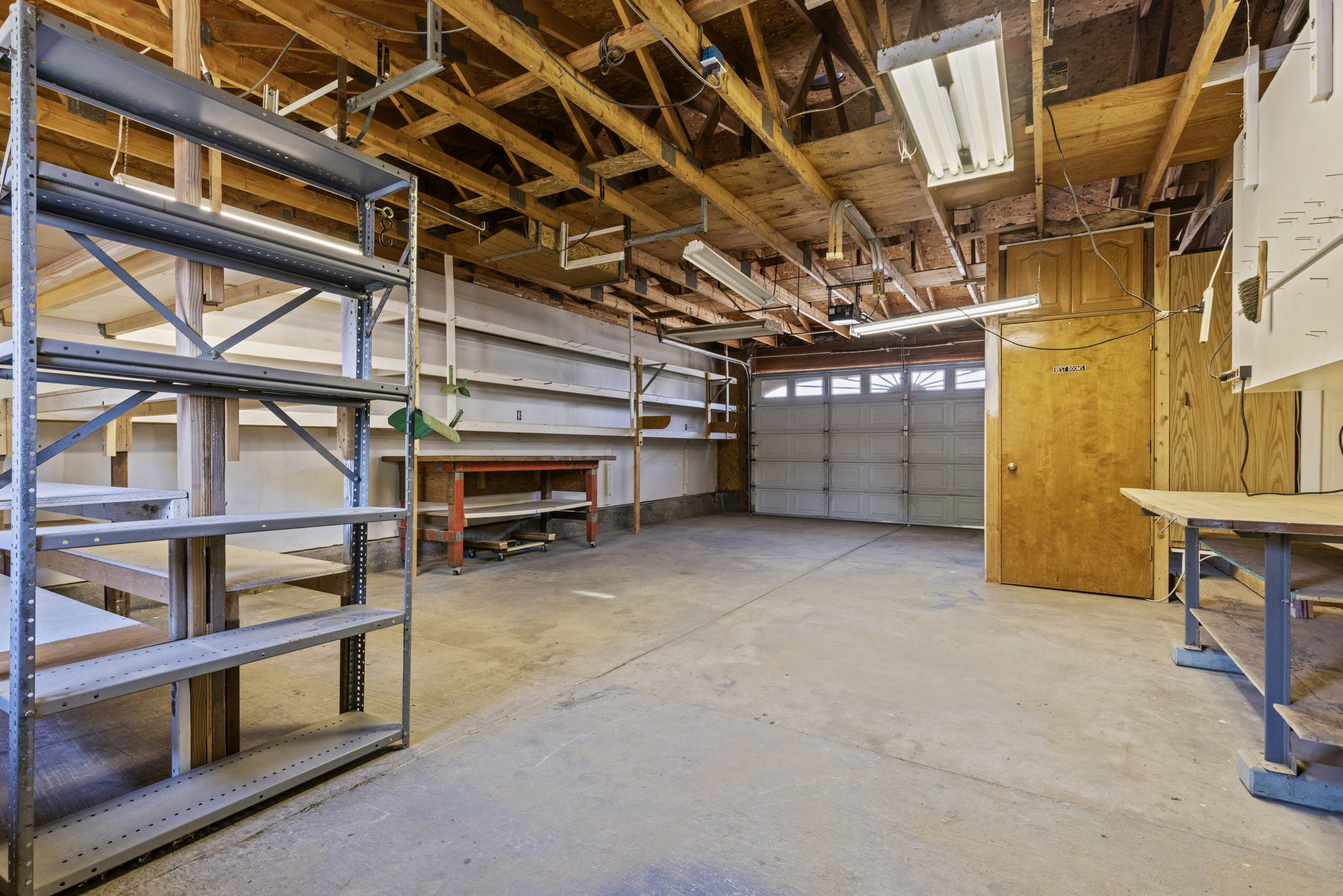 Spacious garage featuring a concrete floor, exposed wood beam ceiling, fluorescent lighting, and a roll-up garage door