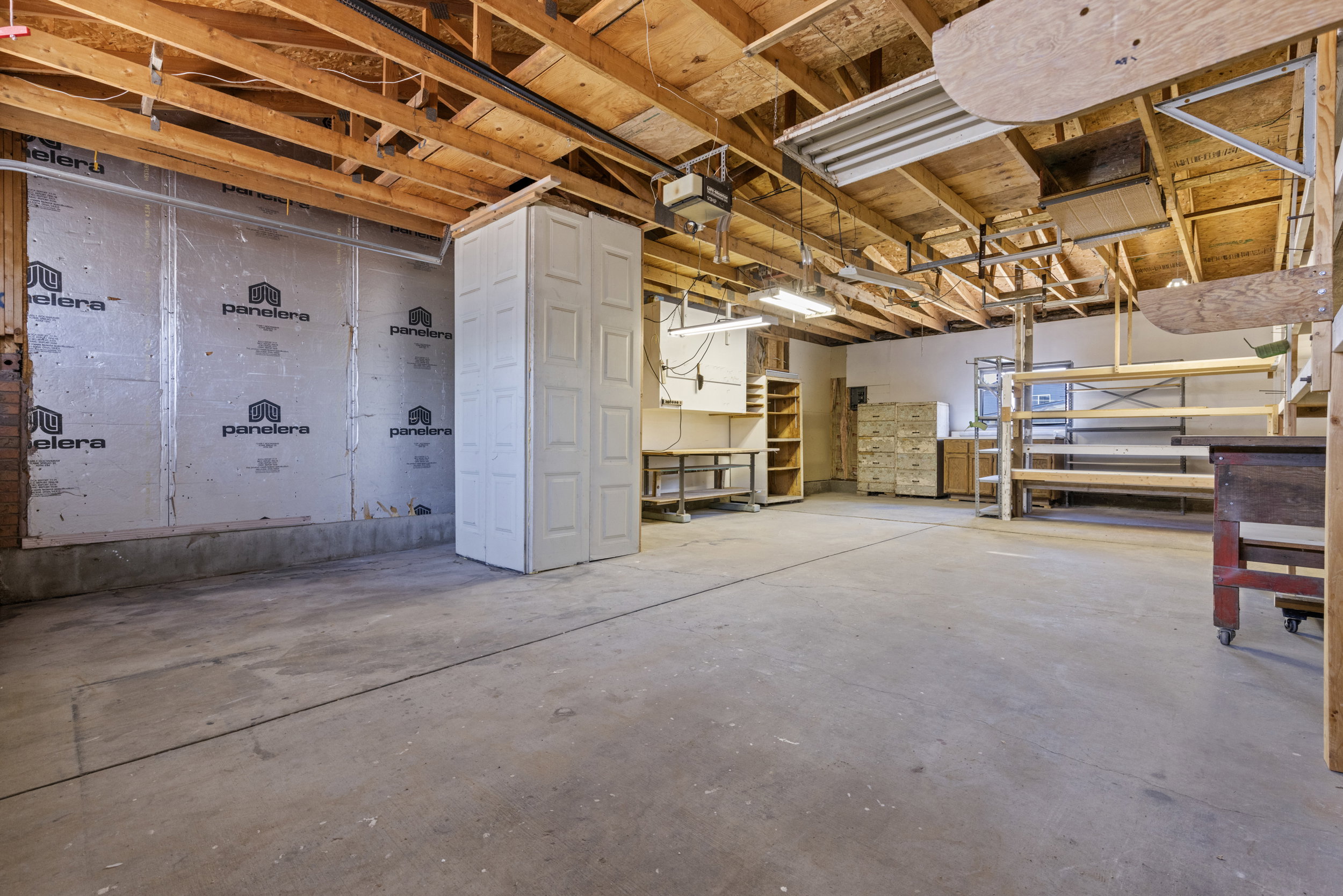 Spacious utility room featuring a concrete floor, exposed wood ceiling joists, and fluorescent lighting