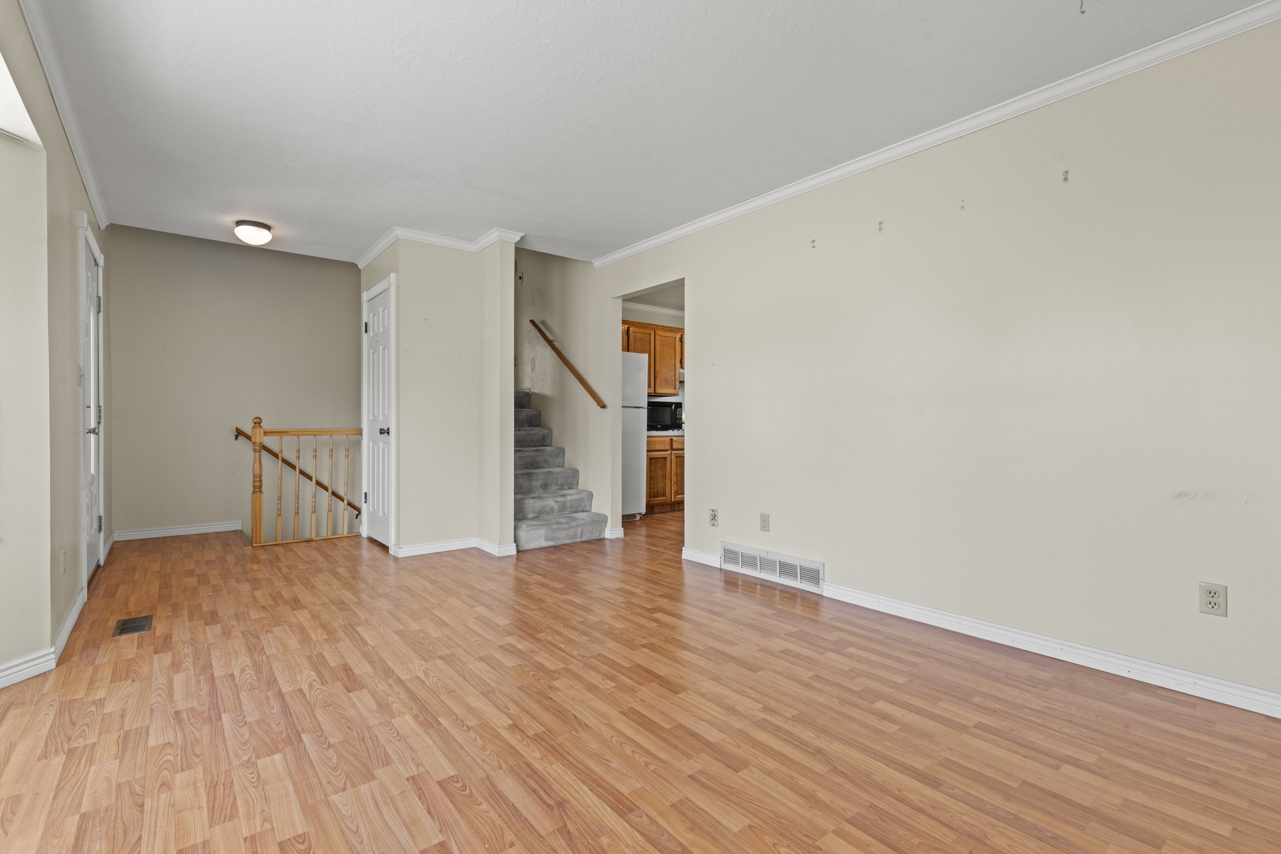 Spacious room with wood-finish flooring, white baseboards, and crown molding