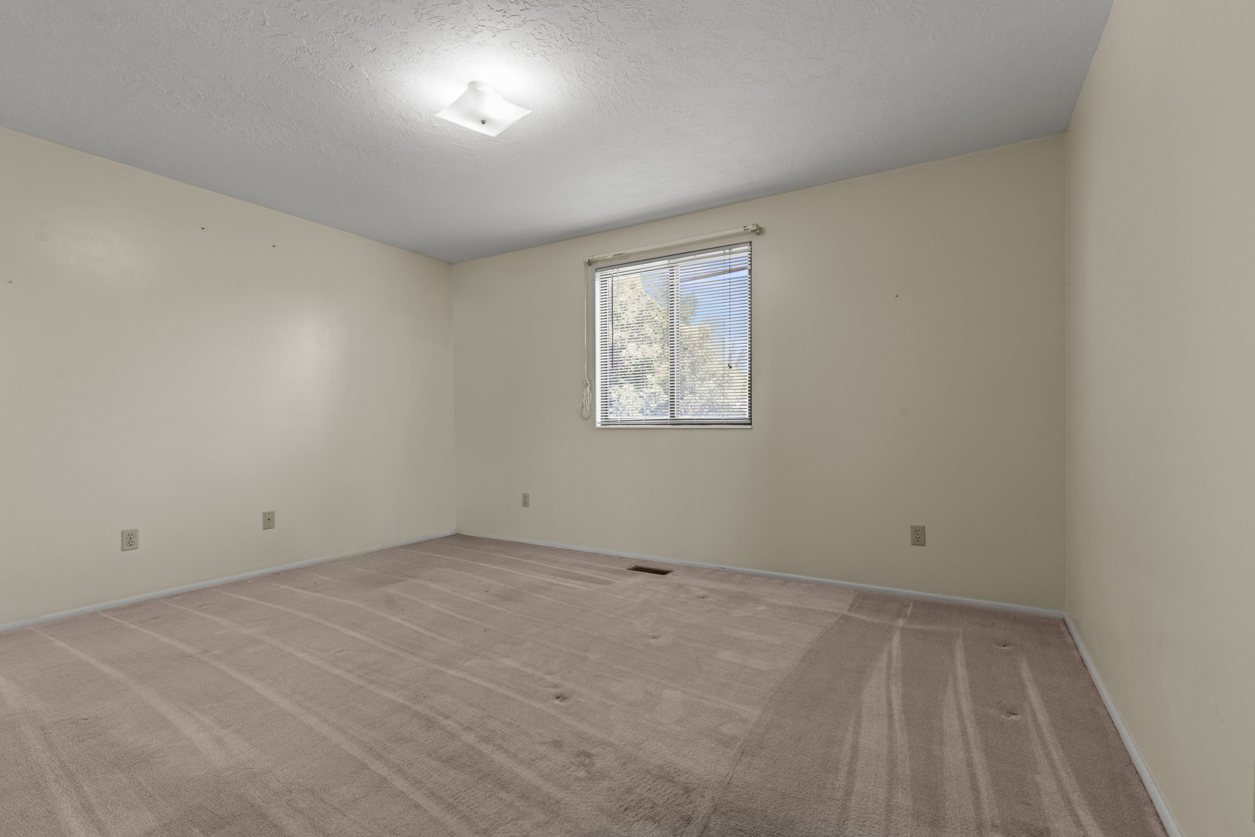 Spacious room featuring neutral wall tones, broadloom carpeting, and a window with blinds