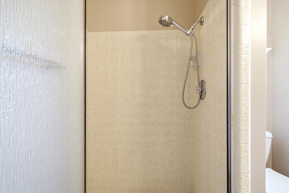 Tiled shower stall featuring a chrome showerhead with a handheld sprayer and a textured glass enclosure