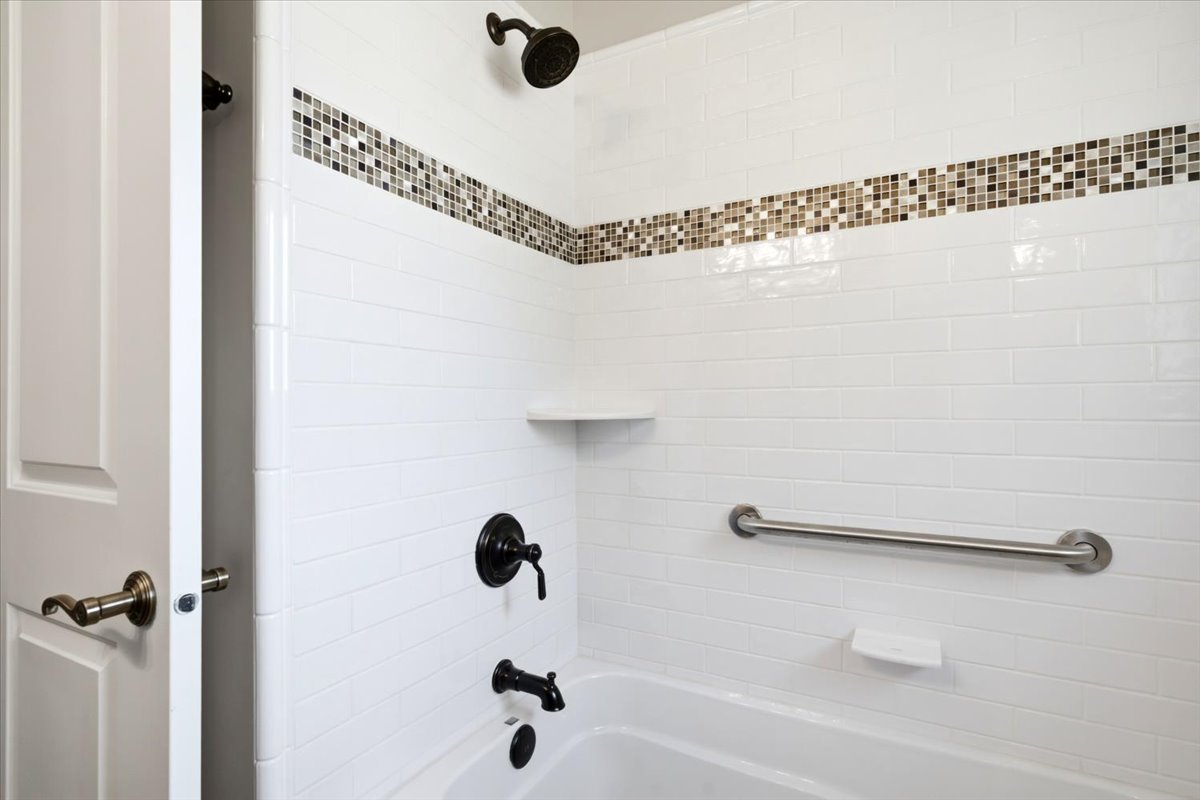 Tub and shower combination featuring white subway tile, a mosaic accent band, oil-rubbed bronze fixtures, and a chrome grab bar