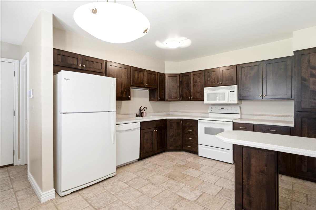 Kitchen featuring dark wood cabinetry, light-toned countertops, tile flooring, and white appliances including a refrigerator, dishwasher, and range