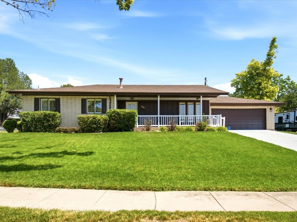 Ranch-style residence featuring a brick facade, covered front porch with white railing, and an attached two-car garage