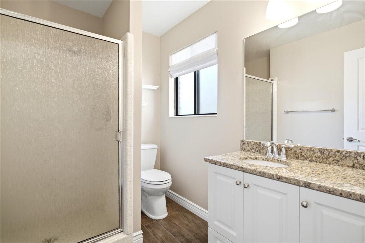 Bathroom featuring a glass-enclosed shower, white vanity with stone-finish countertop, wood-finish flooring, and window with blinds