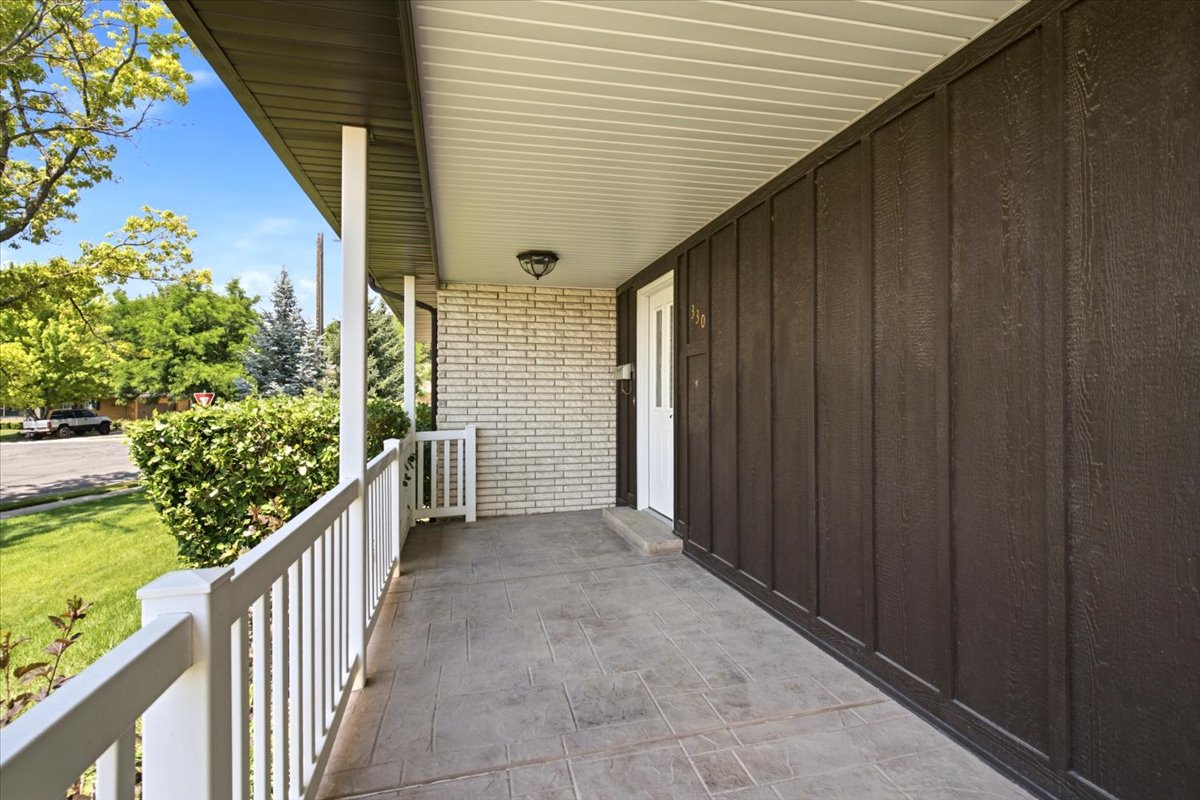 Covered front porch featuring stamped concrete flooring, white railing, and dark vertical siding