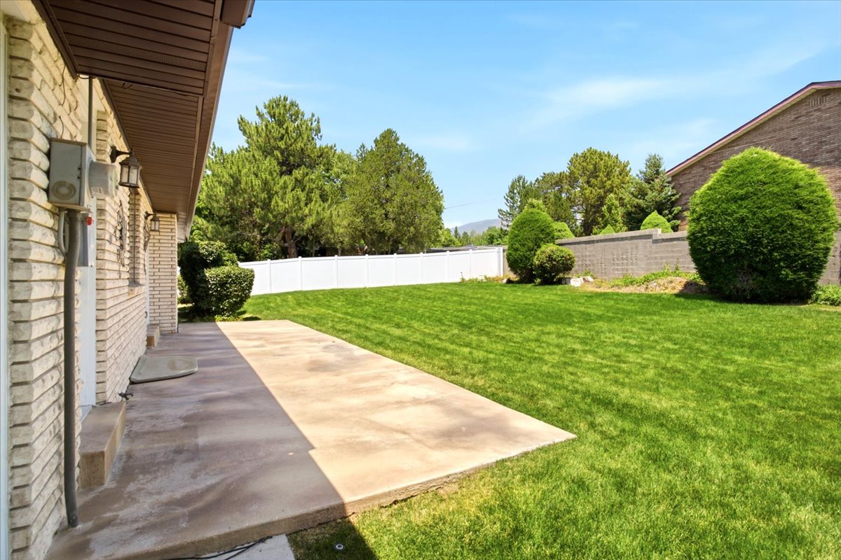 Expansive backyard featuring a manicured lawn, established landscaping, and a concrete patio