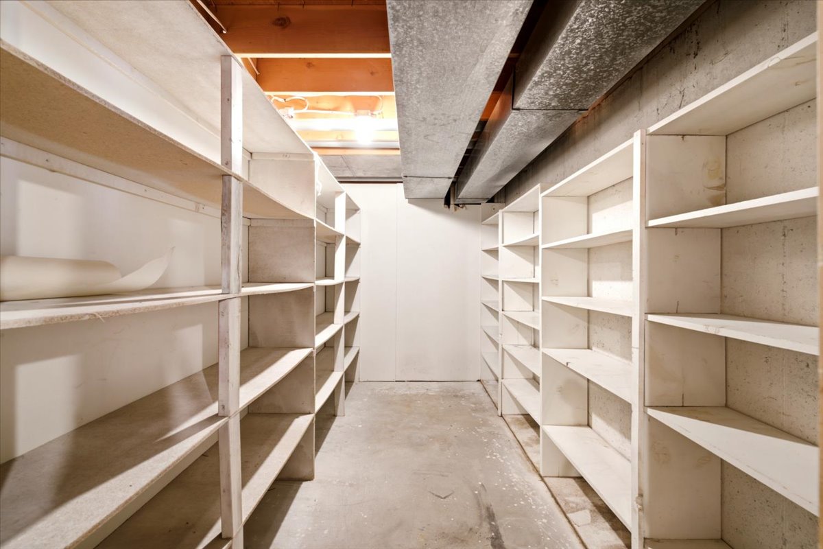 Storage room featuring extensive built-in shelving, exposed ceiling joists, concrete flooring, and an overhead duct system