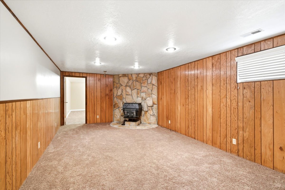 Room featuring a stone fireplace with a wood-burning stove, wood paneling, and recessed lighting