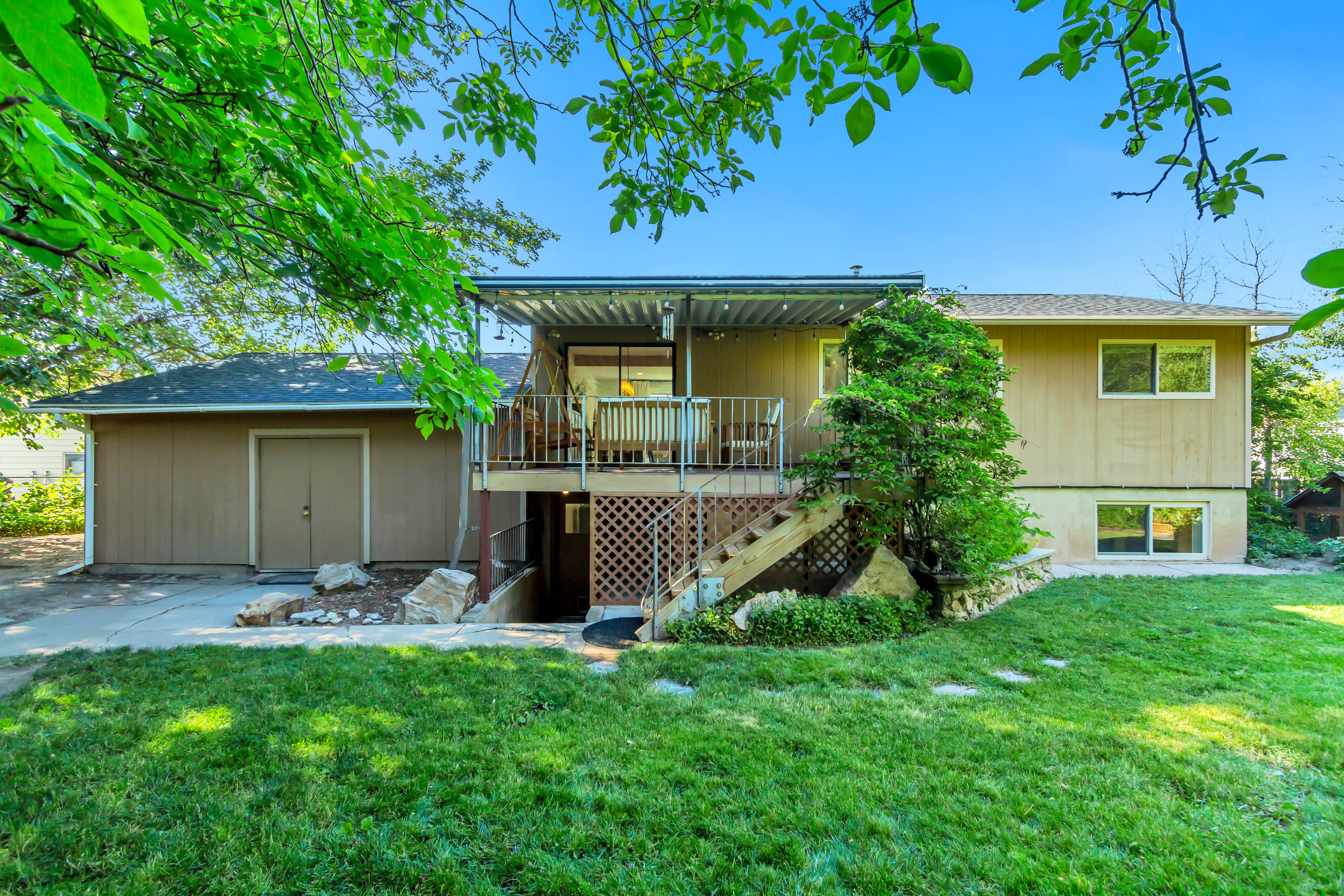 Expansive backyard featuring a manicured lawn, established landscaping, a multi-level deck with a covered patio, and a separate storage structure