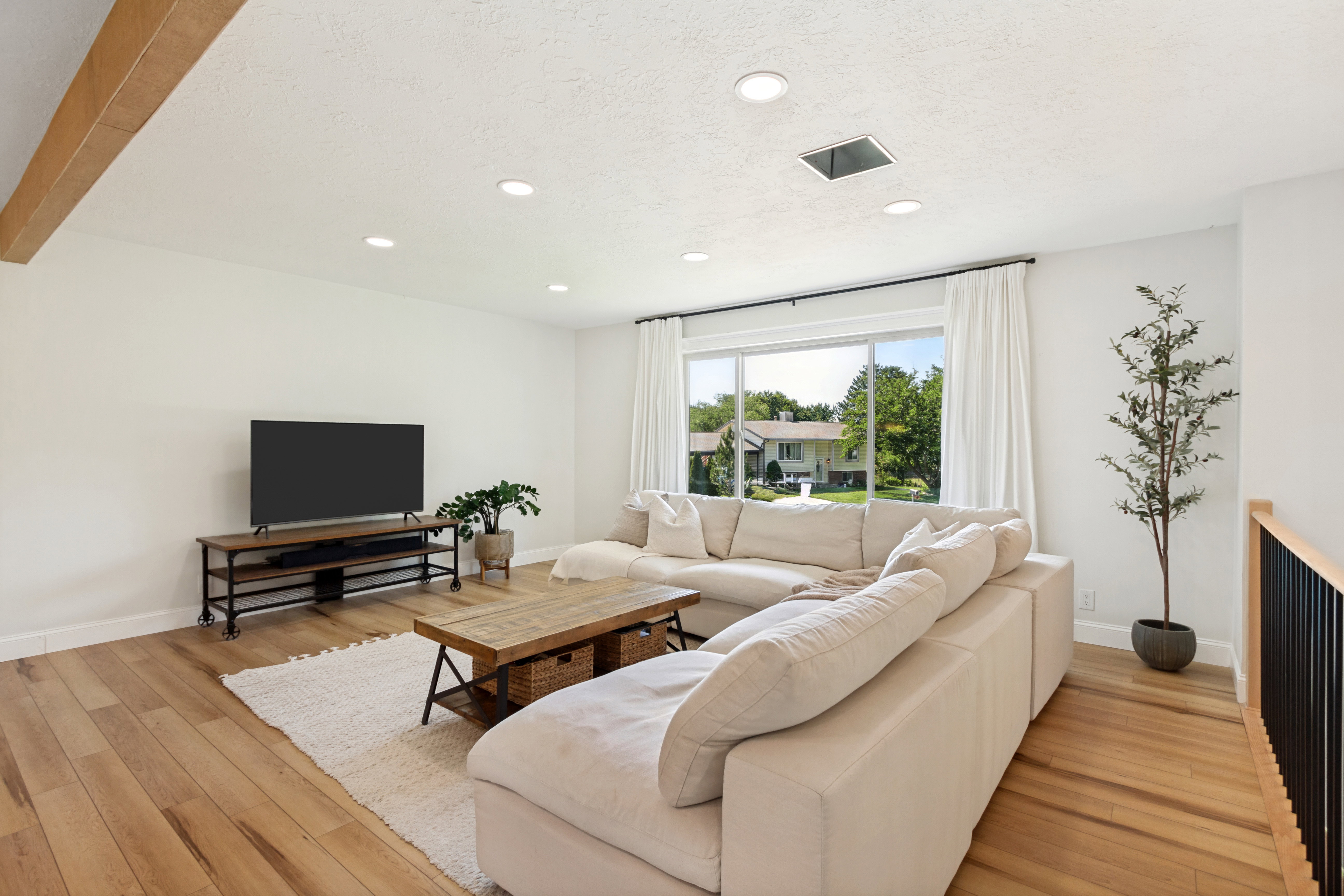 Bright living area with wood-finish flooring, recessed lighting, and a large picture window