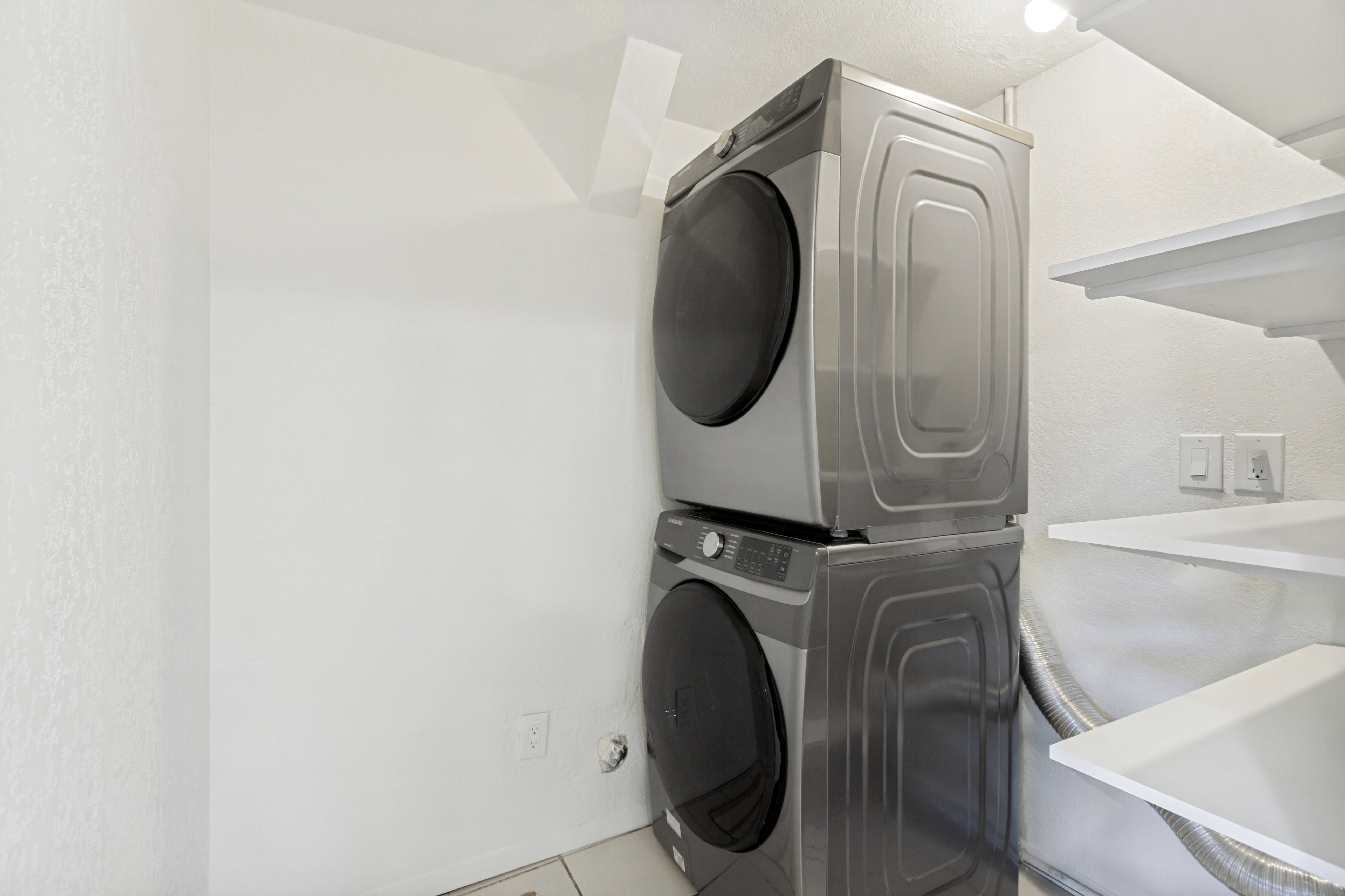 Dedicated laundry space featuring a stacked washer and dryer, white shelving, and tile flooring