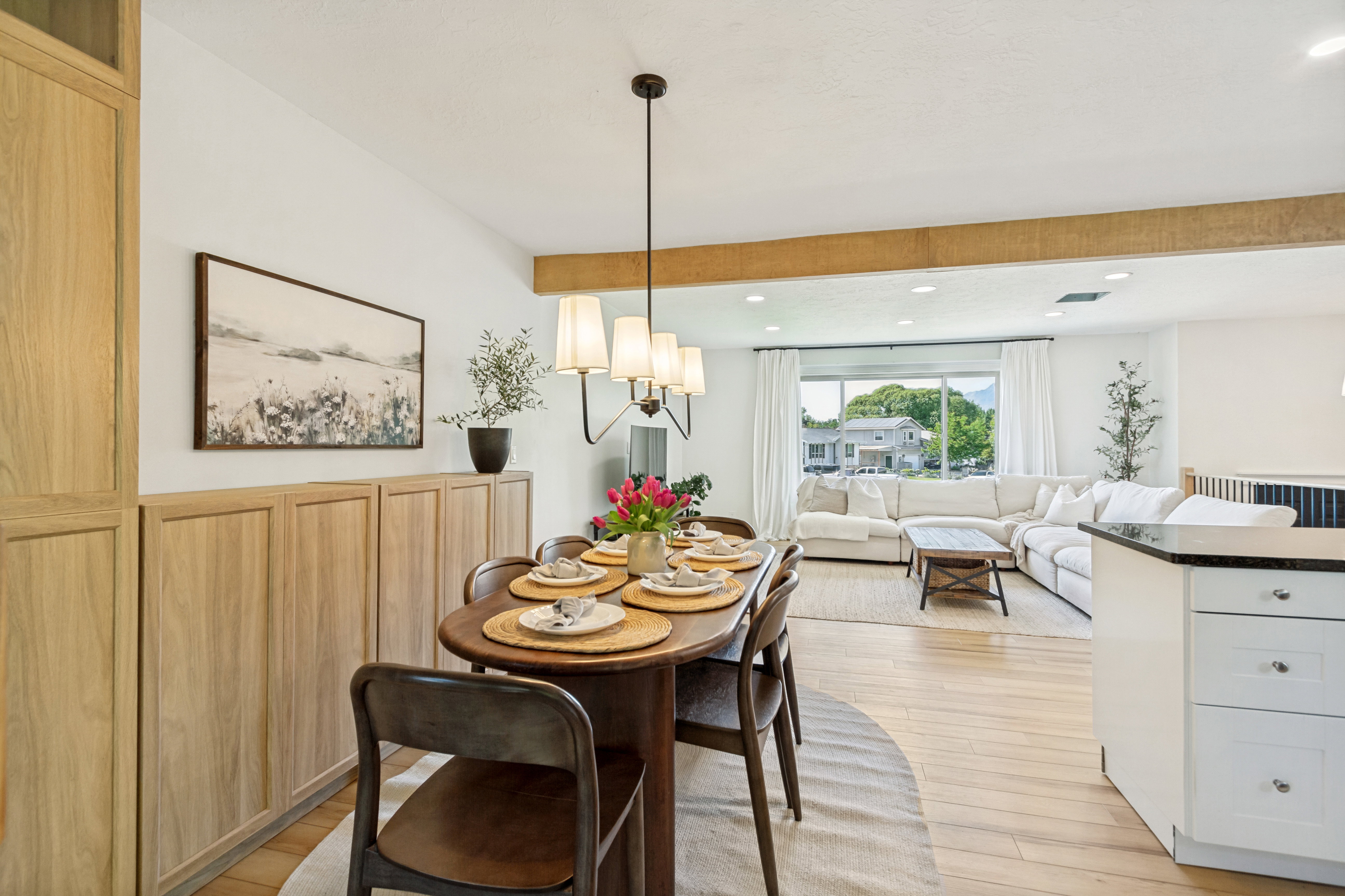 Open-concept living space featuring wood-finish flooring, a contemporary chandelier, built-in cabinetry, and a prominent wood beam accent