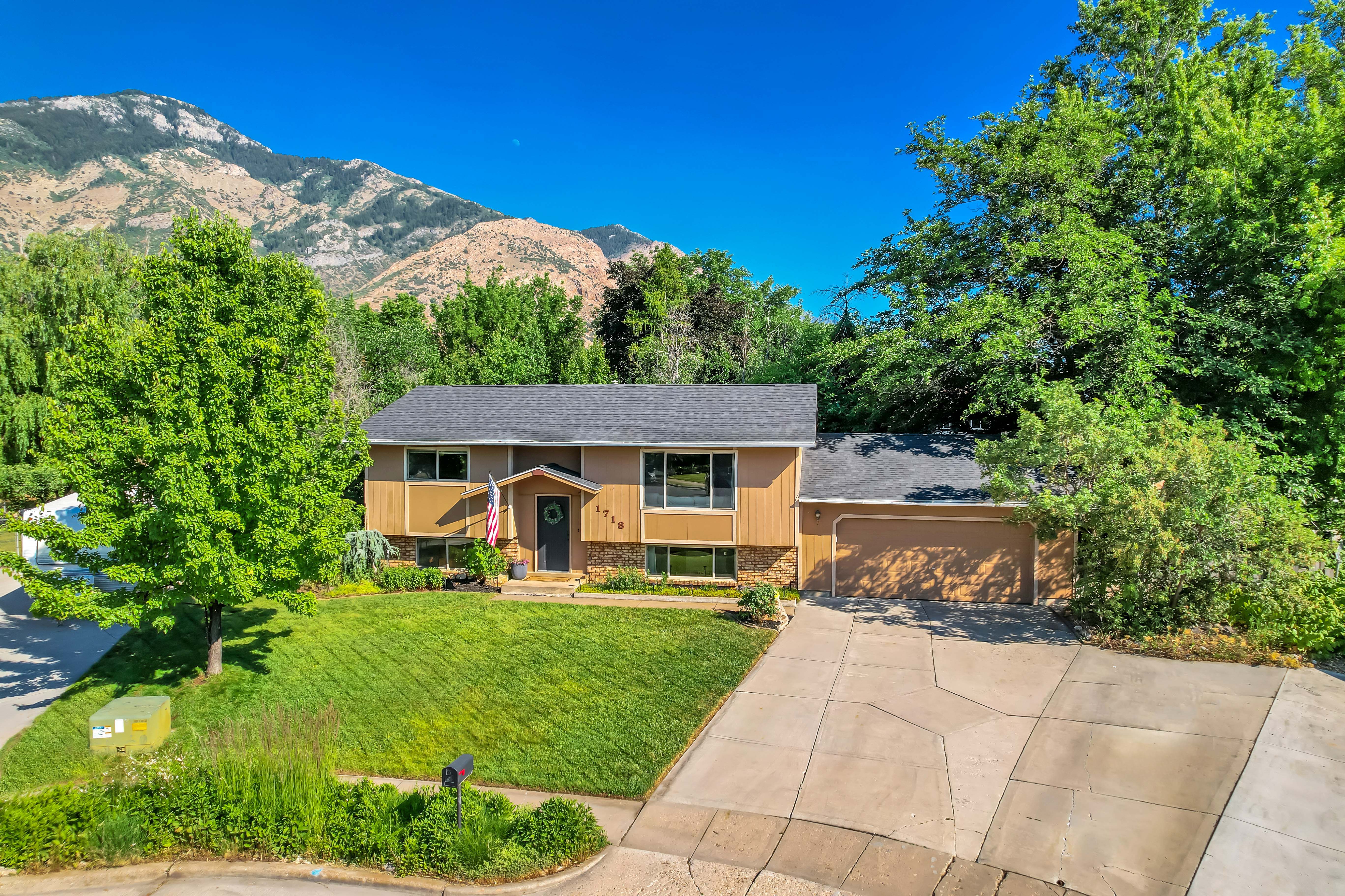 Split-level residence featuring a two-car garage, a well-maintained front lawn, and mature trees