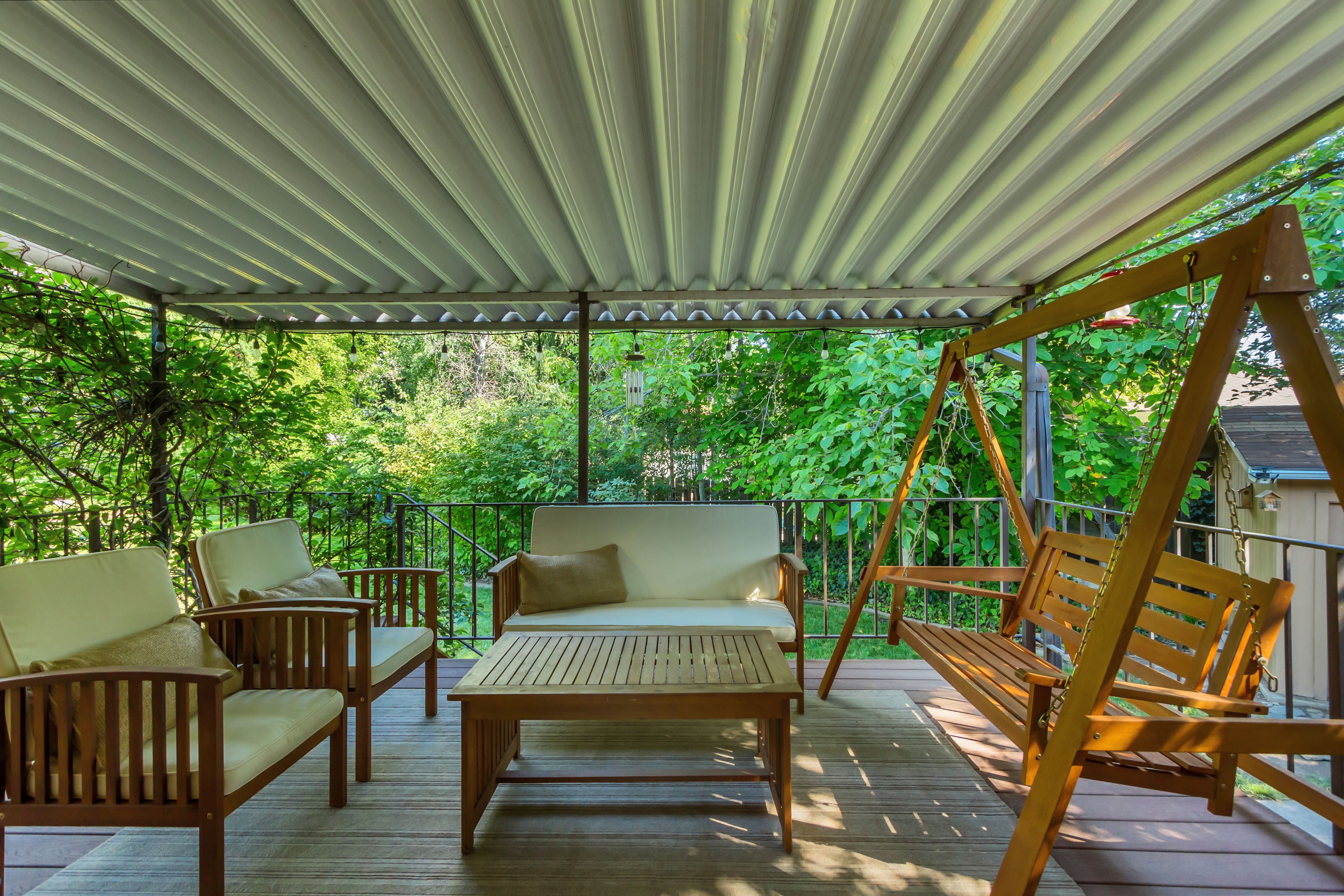 Covered outdoor patio featuring a slatted ceiling, dark wood-finish decking, and a black metal railing