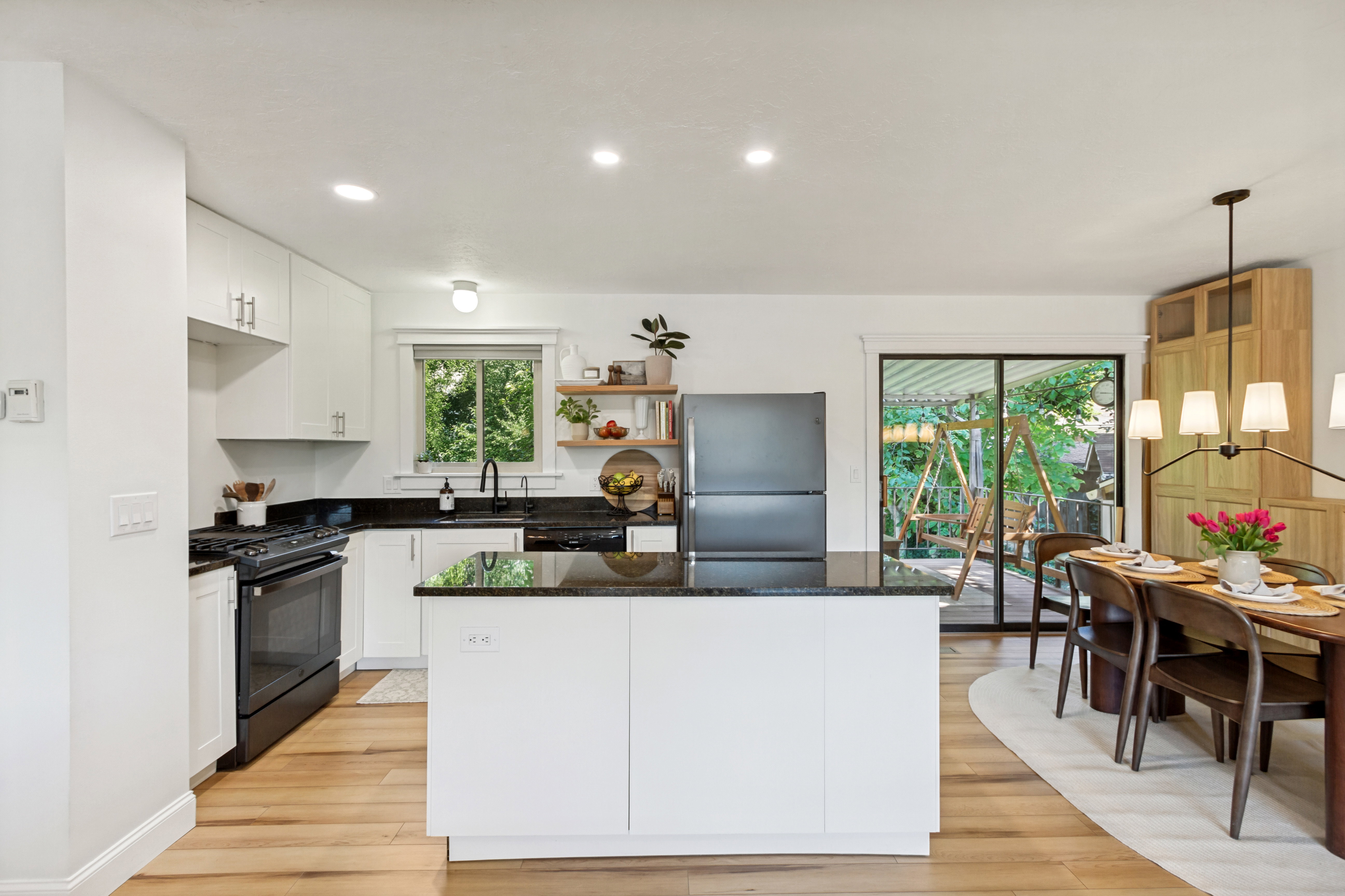 Kitchen featuring white cabinetry, black stone countertops, wood-finish flooring, a central island, and sliding glass doors to the exterior