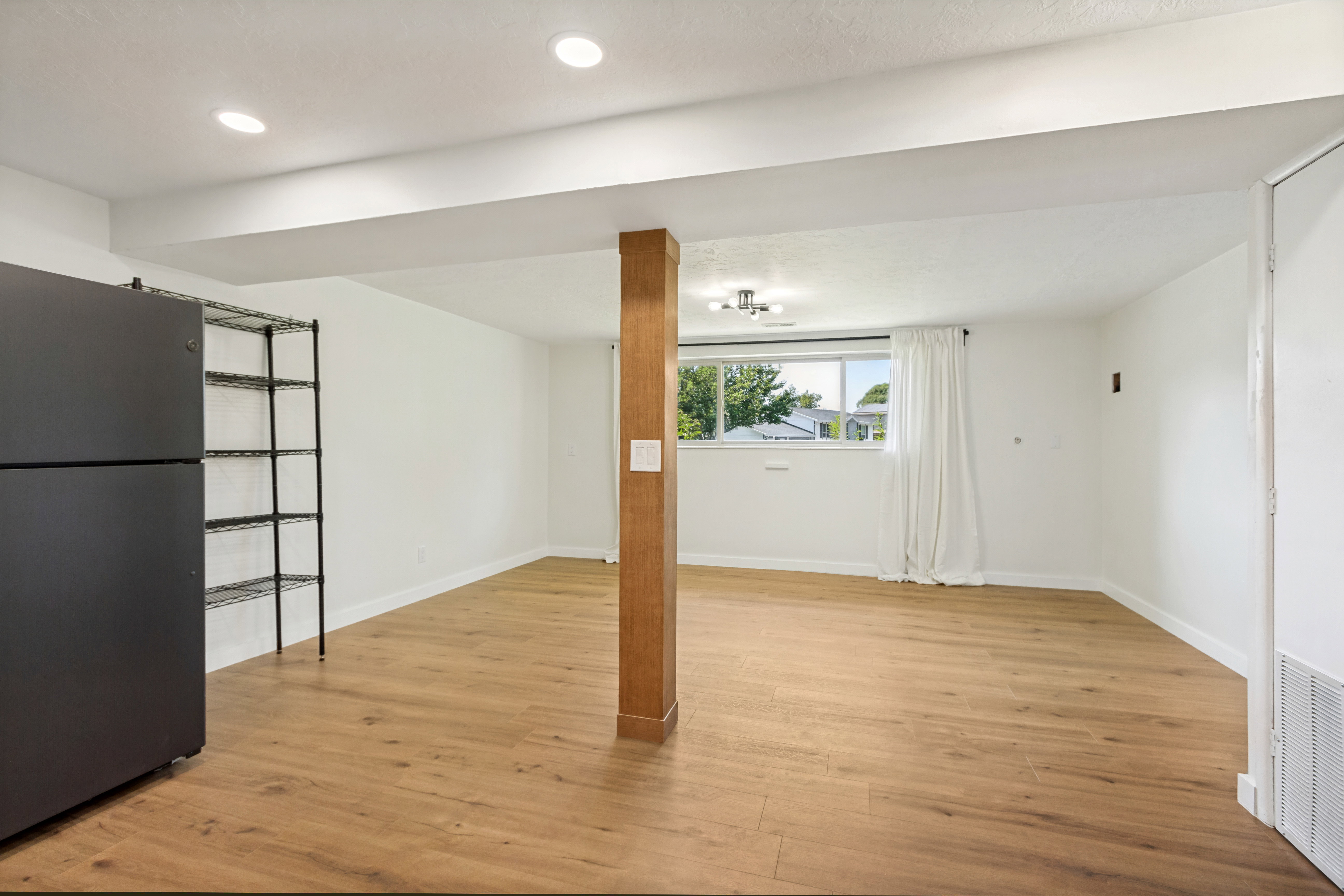 Spacious room featuring wood-finish flooring, white walls, and a visible window for natural light