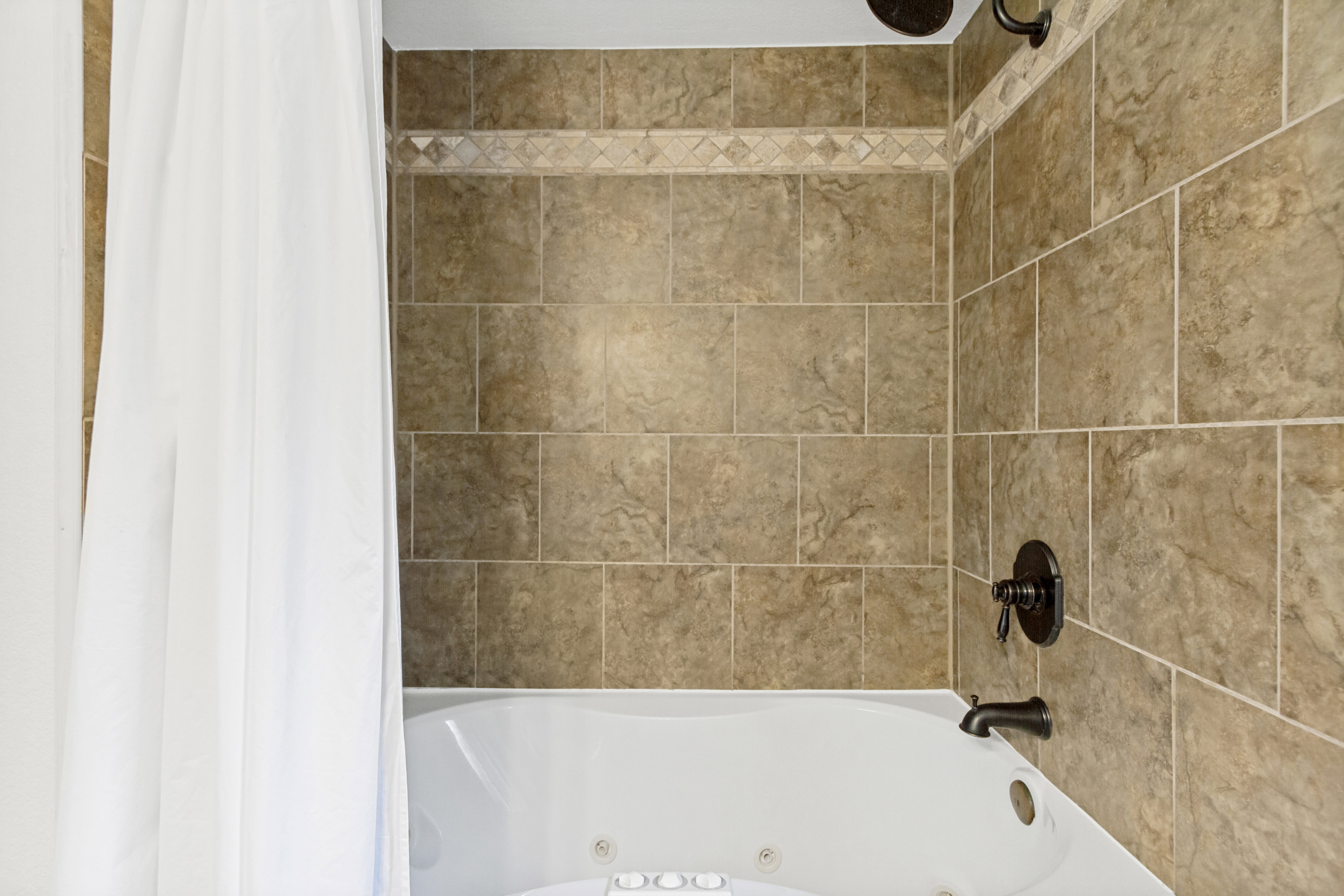 Soaking tub with integrated jets and bronze fixtures, surrounded by large format wall tile