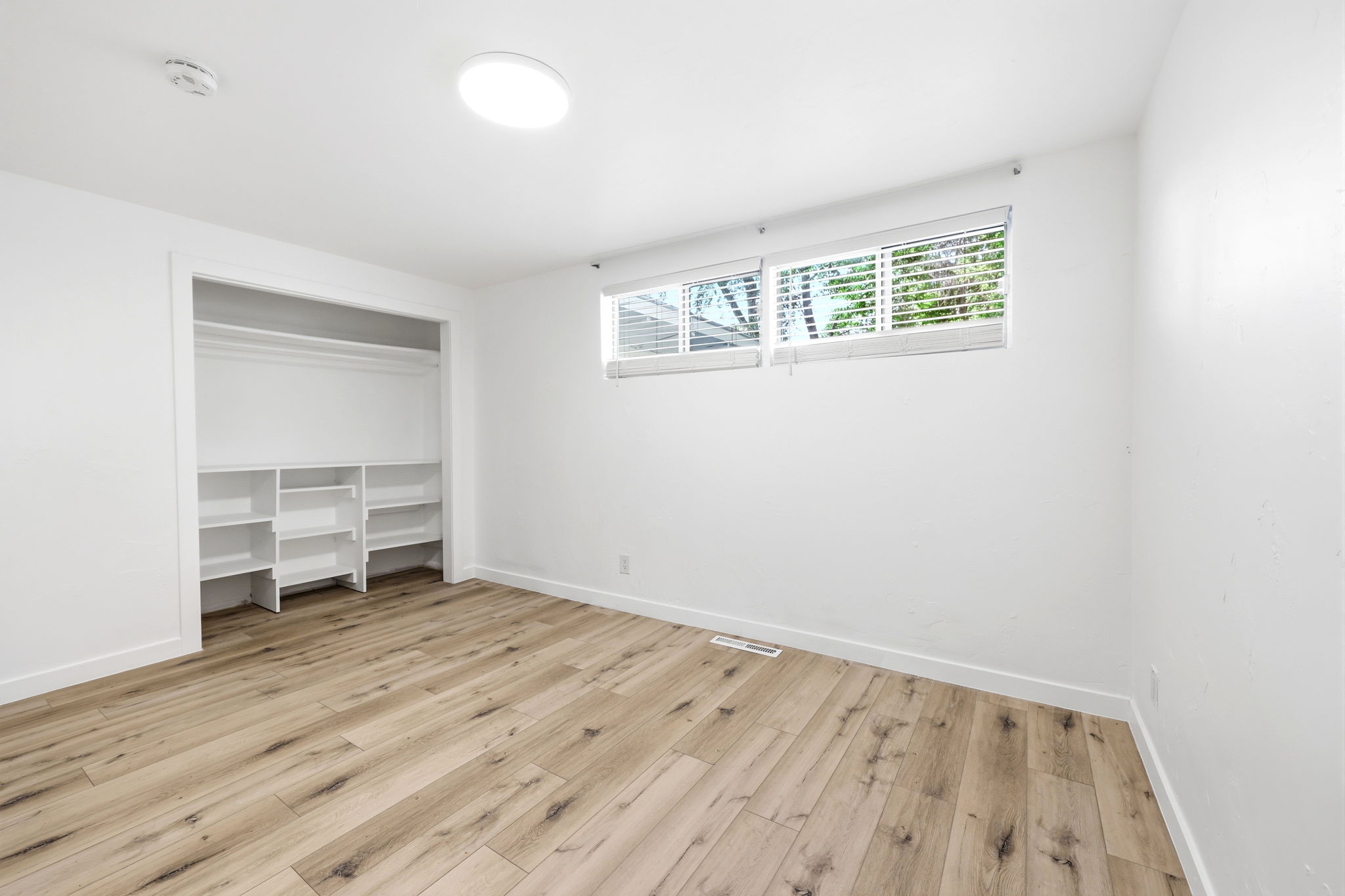 Room featuring wood-finish flooring, white walls, and a recessed window with blinds