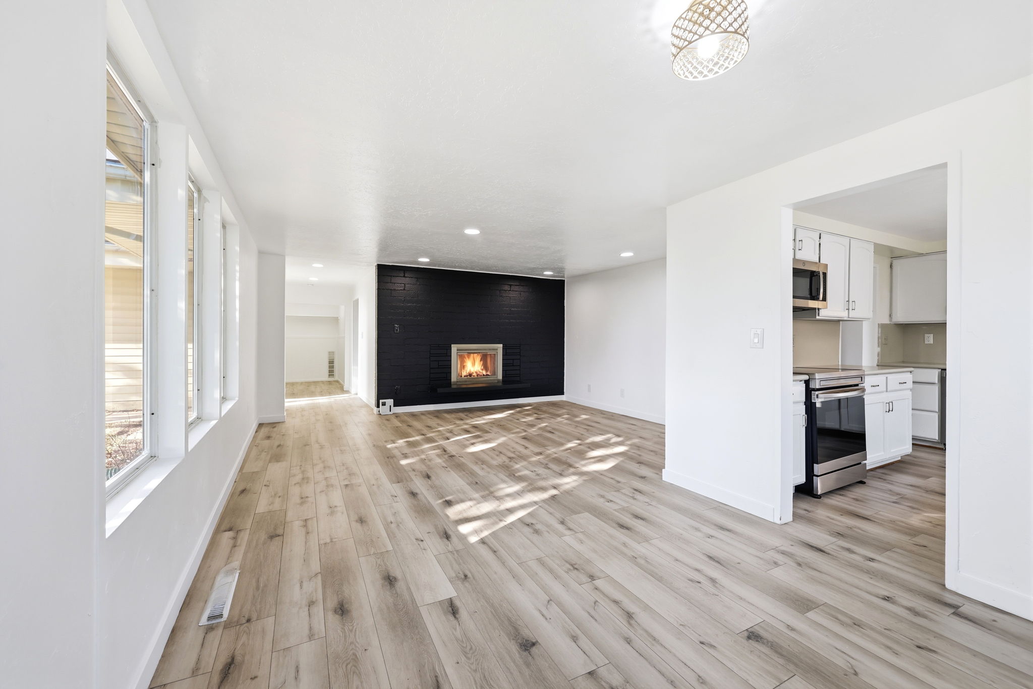 Spacious living area featuring light wood-finish flooring, a prominent black brick fireplace, and recessed lighting