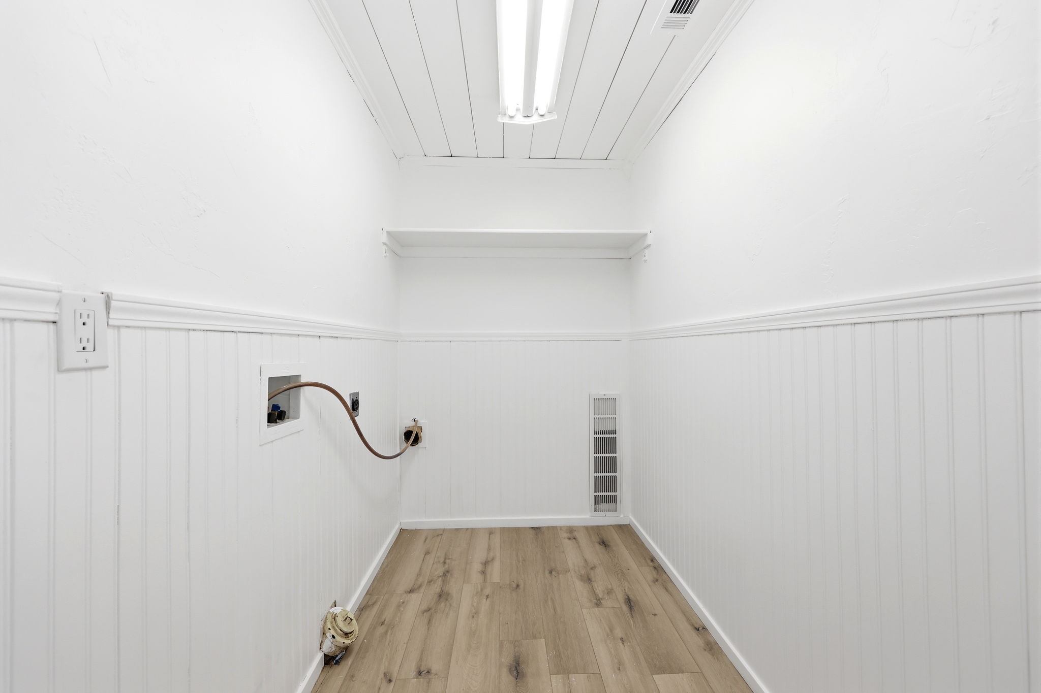 Utility room featuring wood-finish flooring, white beadboard paneling, and a recessed wall shelf