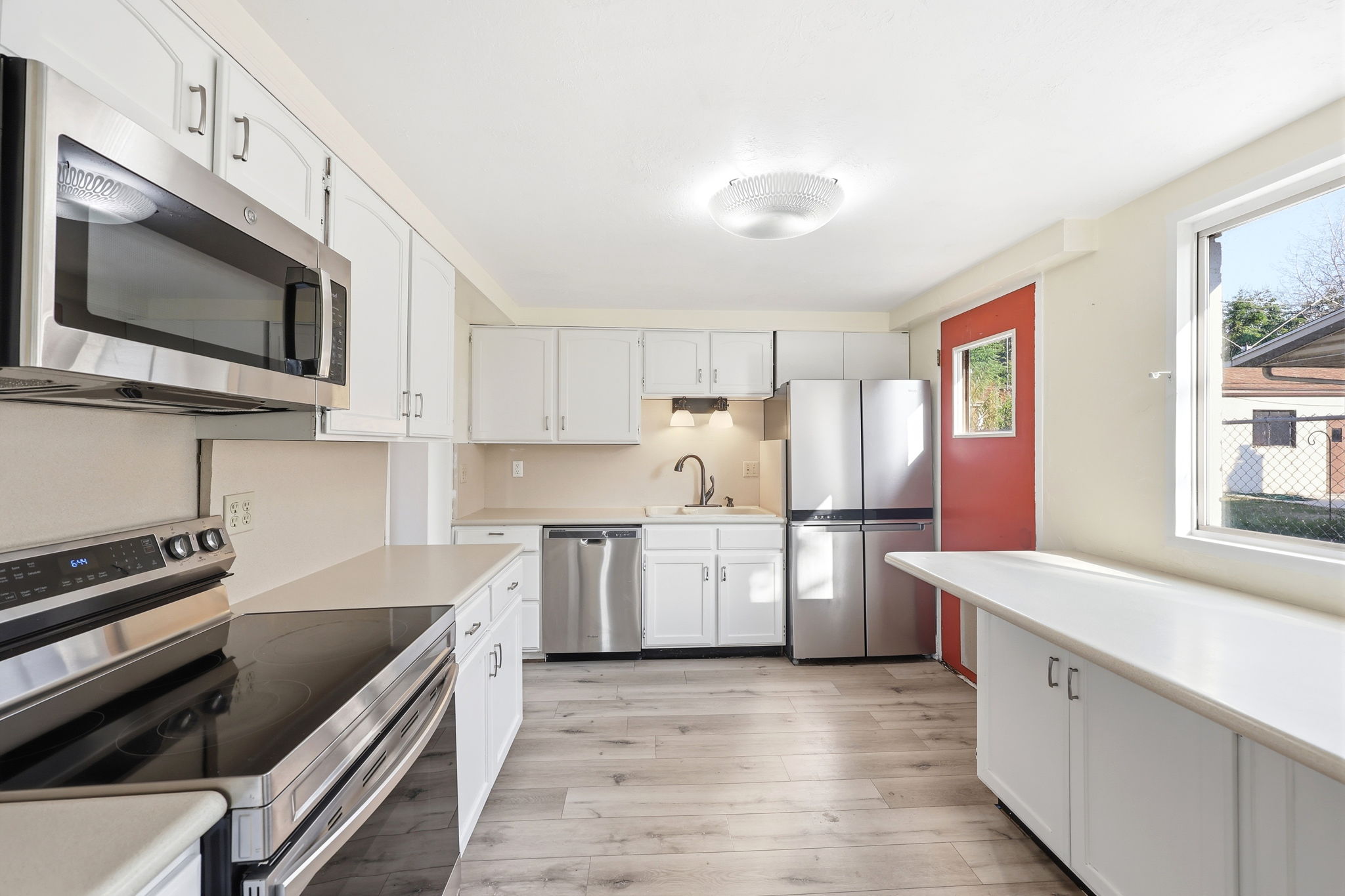 Kitchen featuring white cabinetry, light countertops, wood-finish flooring, stainless steel appliances, and a red door