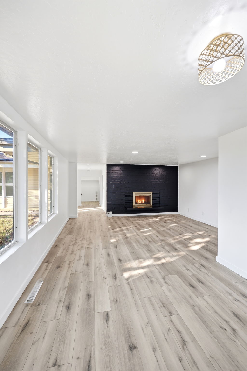 Spacious interior featuring wide-plank wood-finish flooring, a contemporary fireplace with a dark brick surround, and a series of large windows