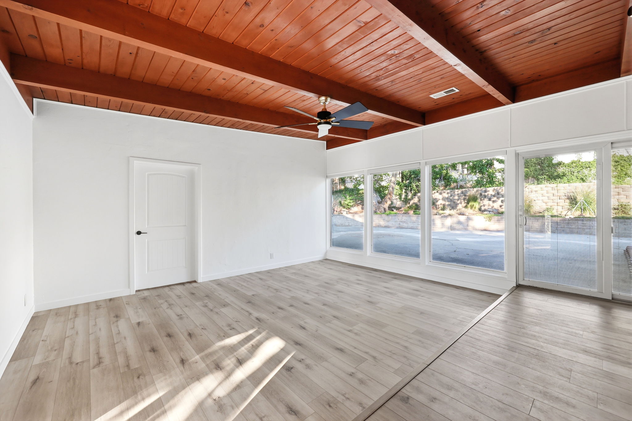 Spacious interior featuring wood-finish flooring, white walls, and an exposed beam wood-paneled ceiling