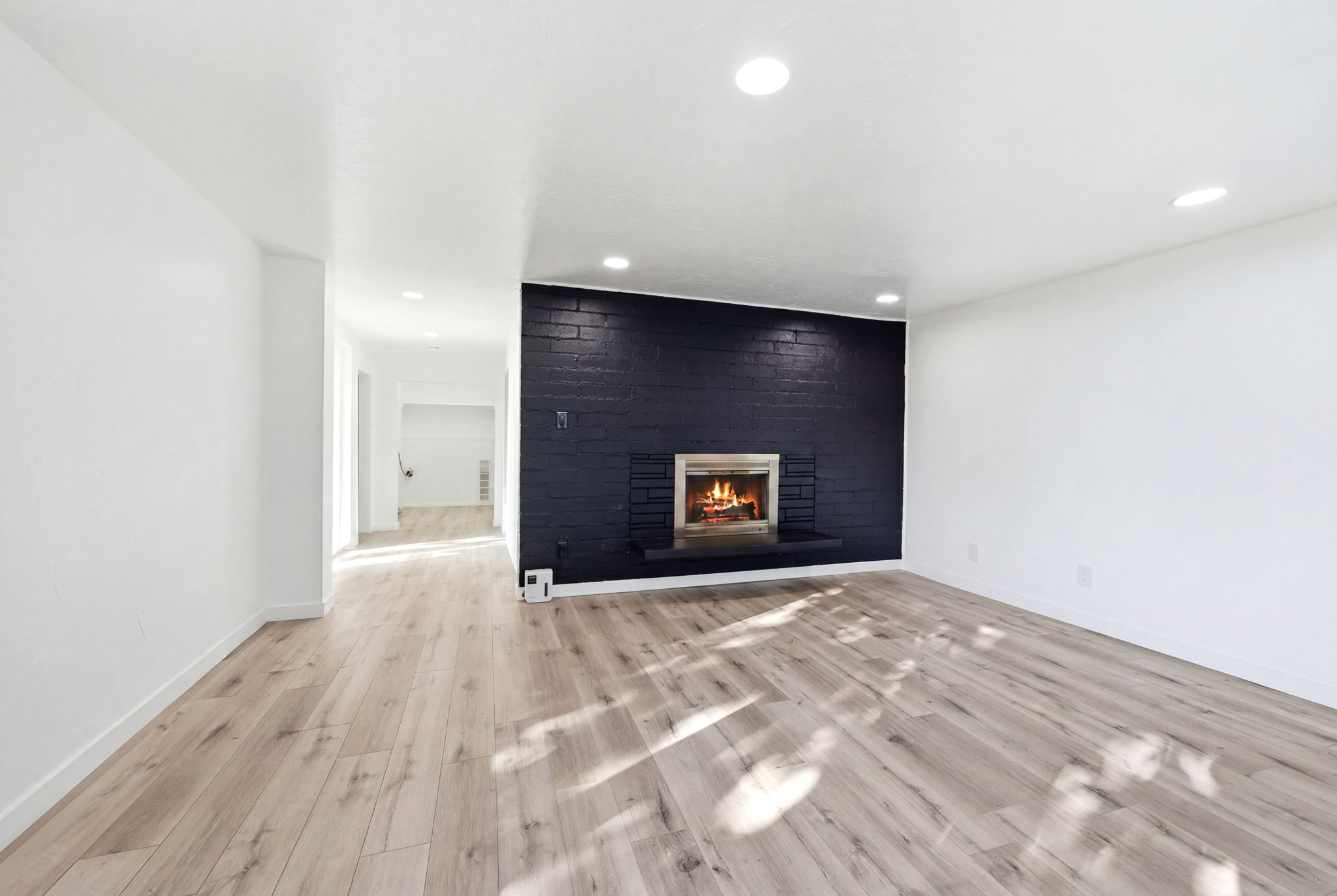 Spacious room featuring a brick fireplace with a dark finish, a light wood-finish flooring, recessed lighting, and bright white walls