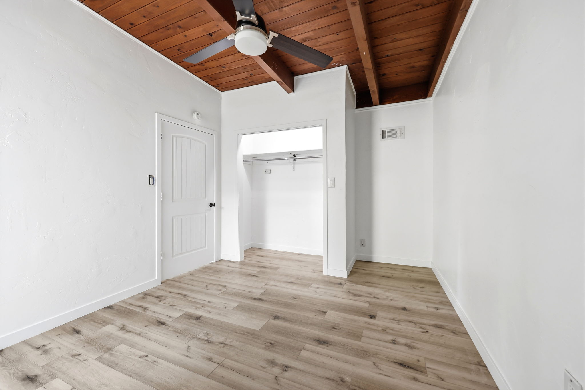 Interior room featuring wood-finish flooring, white painted walls, and a wood-beam ceiling