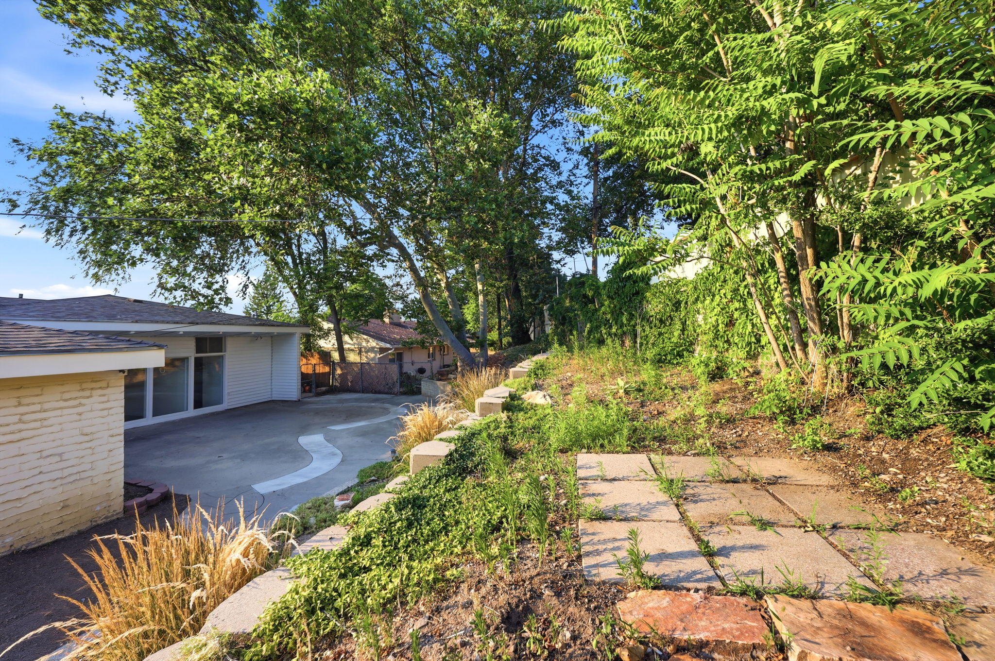 Expansive concrete patio with a decorative inlay, surrounded by mature trees providing natural shade