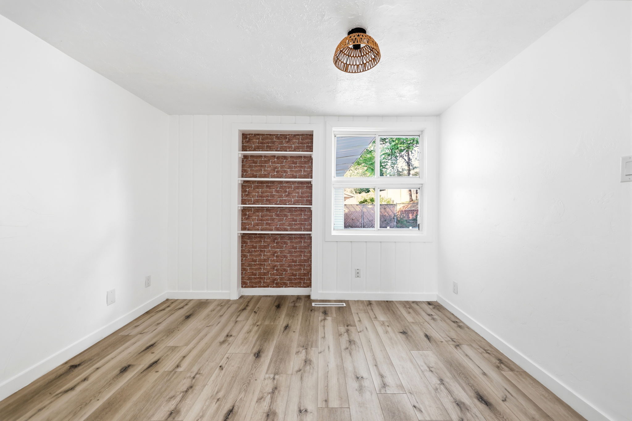 Room featuring wood-finish flooring, white walls, and a built-in shelving unit with a brick-patterned back